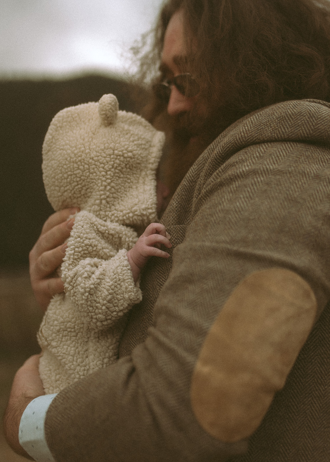A father with long hair cradles his baby against his chest in a cozy onesie with a hood after visiting pediatricians in Hamilton, MT