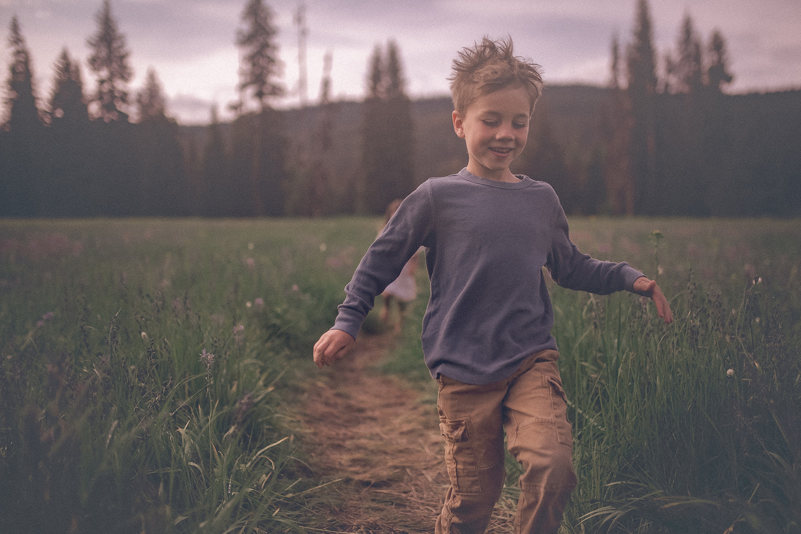 A young boy in a blue shirt and khaki pants runs a meadow trail with sister