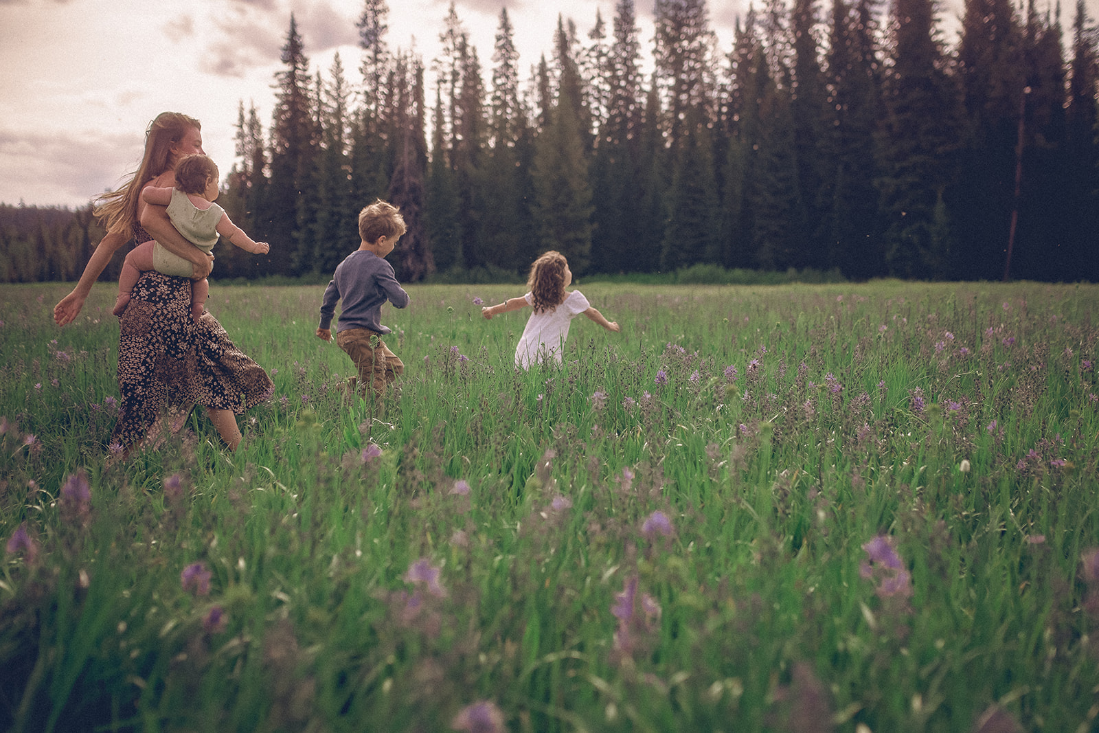 Two happy toddlers run through a field of wildflowers with mom carrying an infant after visiting Yours Mine And Ours Kid Store