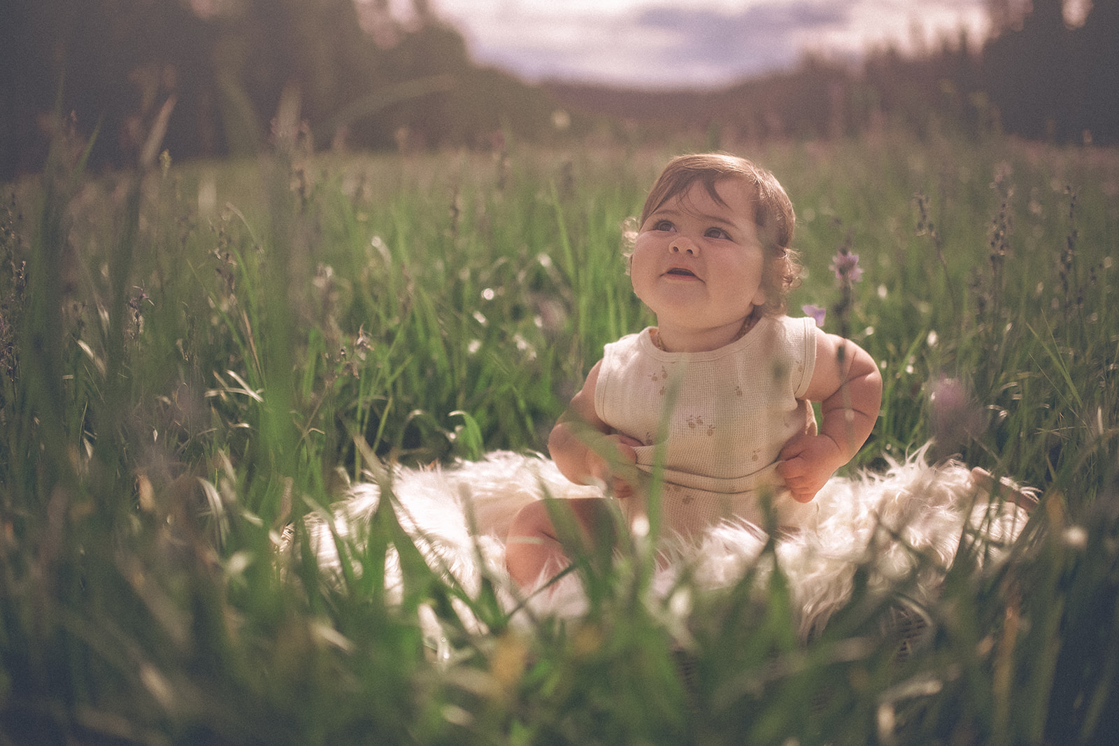 A happy baby in a onesie sits on a blanket in a meadow of wildflowers after visiting Bitterroot Discovery Children's Museum