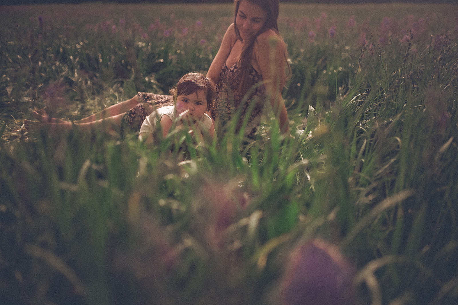 A mom watches as her baby crawls in a field of wildflowers after visiting Bitterroot Discovery Children's Museum