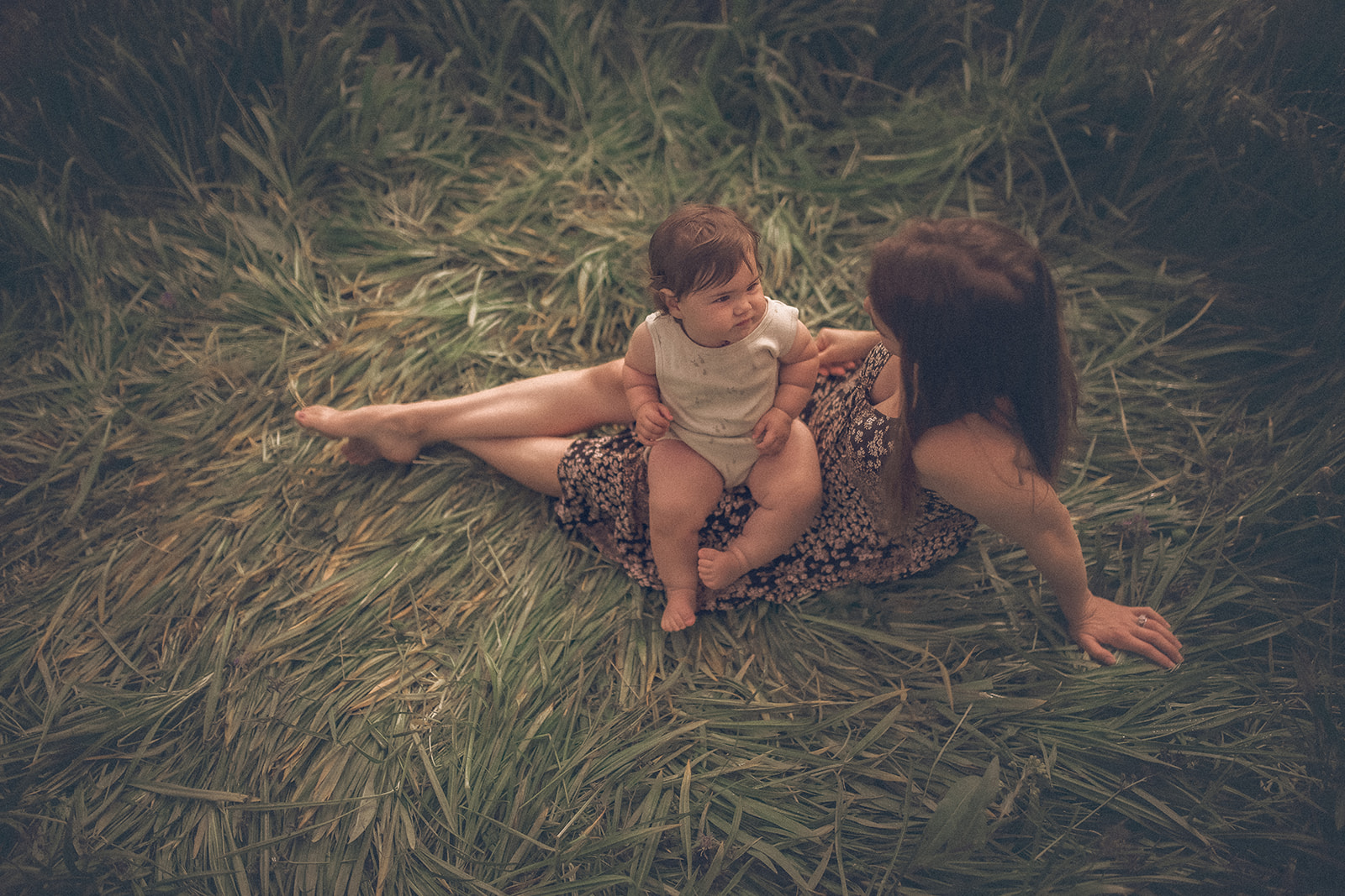 A look down on an infant sitting in mom's lap in a patch of laid down grasses after some baby music classes in Hamilton, MT