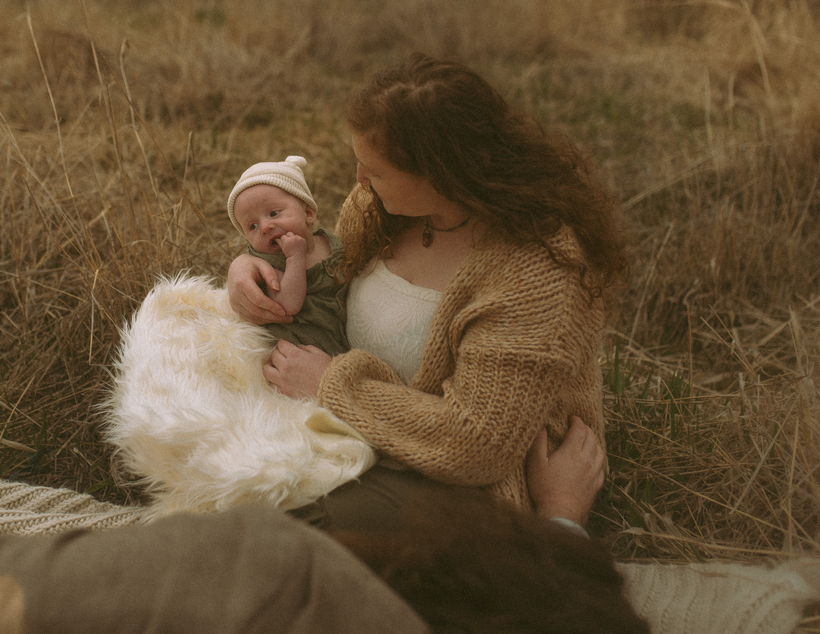 A happy mom snuggles her infant on a picnic blanket in tall golden grass in a knit sweater after visiting baby shower venues in Hamilton, MT