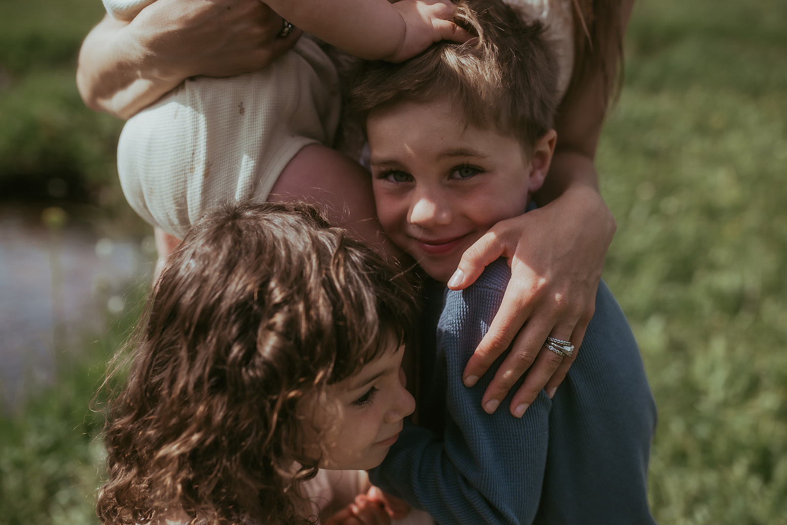 Toddler boy and girl siblings hug mom in a meadow