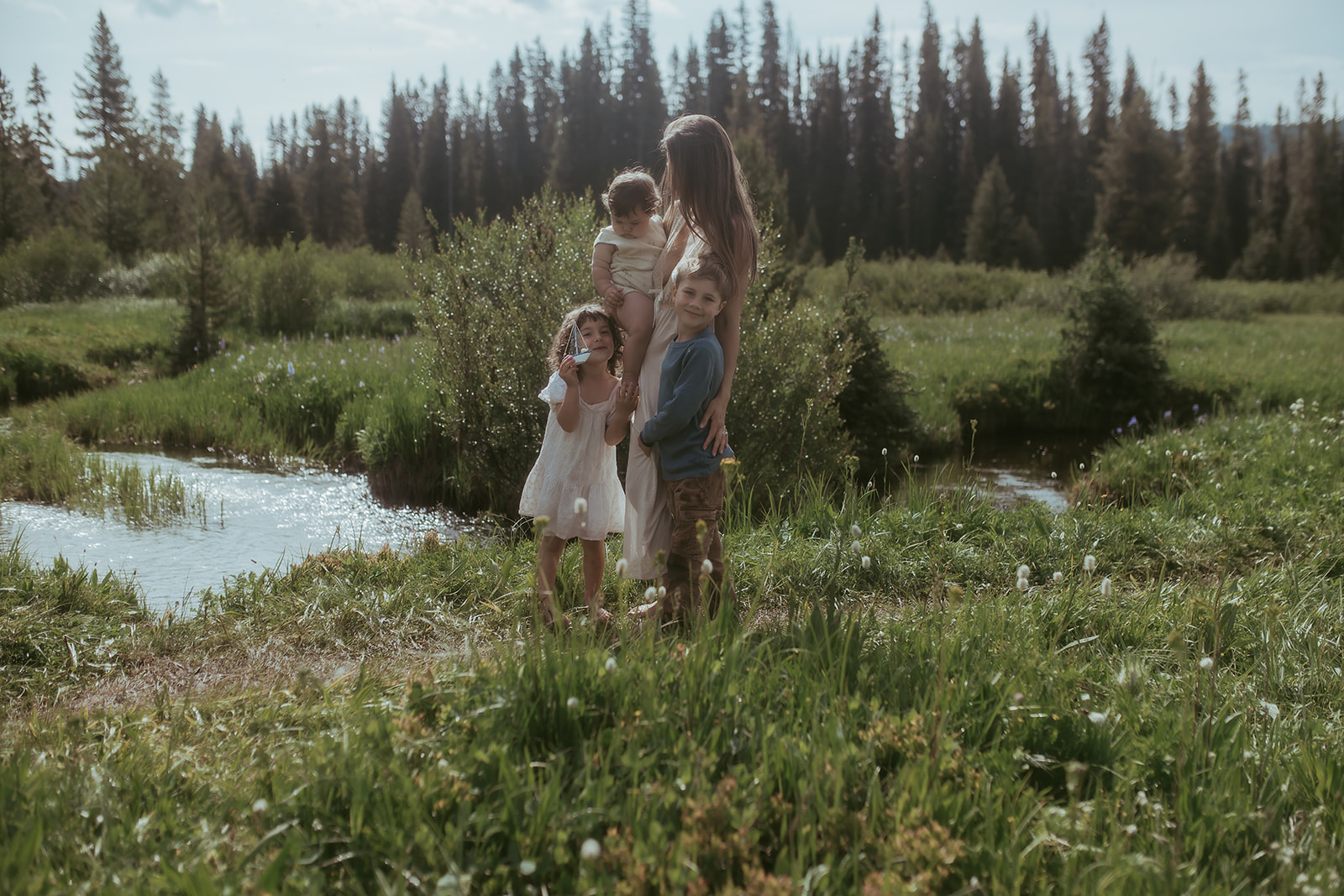 A mother stands by a creek holding a baby with her two toddlers after visiting birthday party places in Hamilton, MT