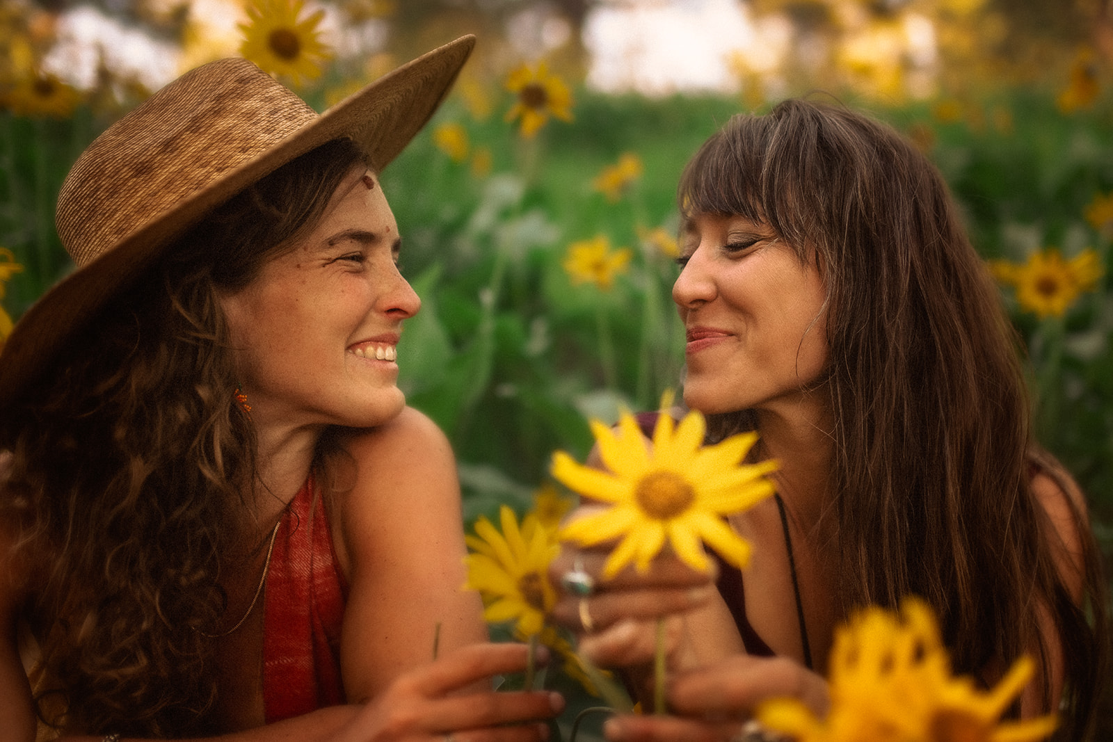 Two women lay in a bed of yellow flowers smiling at each other with one in a large hat after some parenting classes in Hamilton, MT