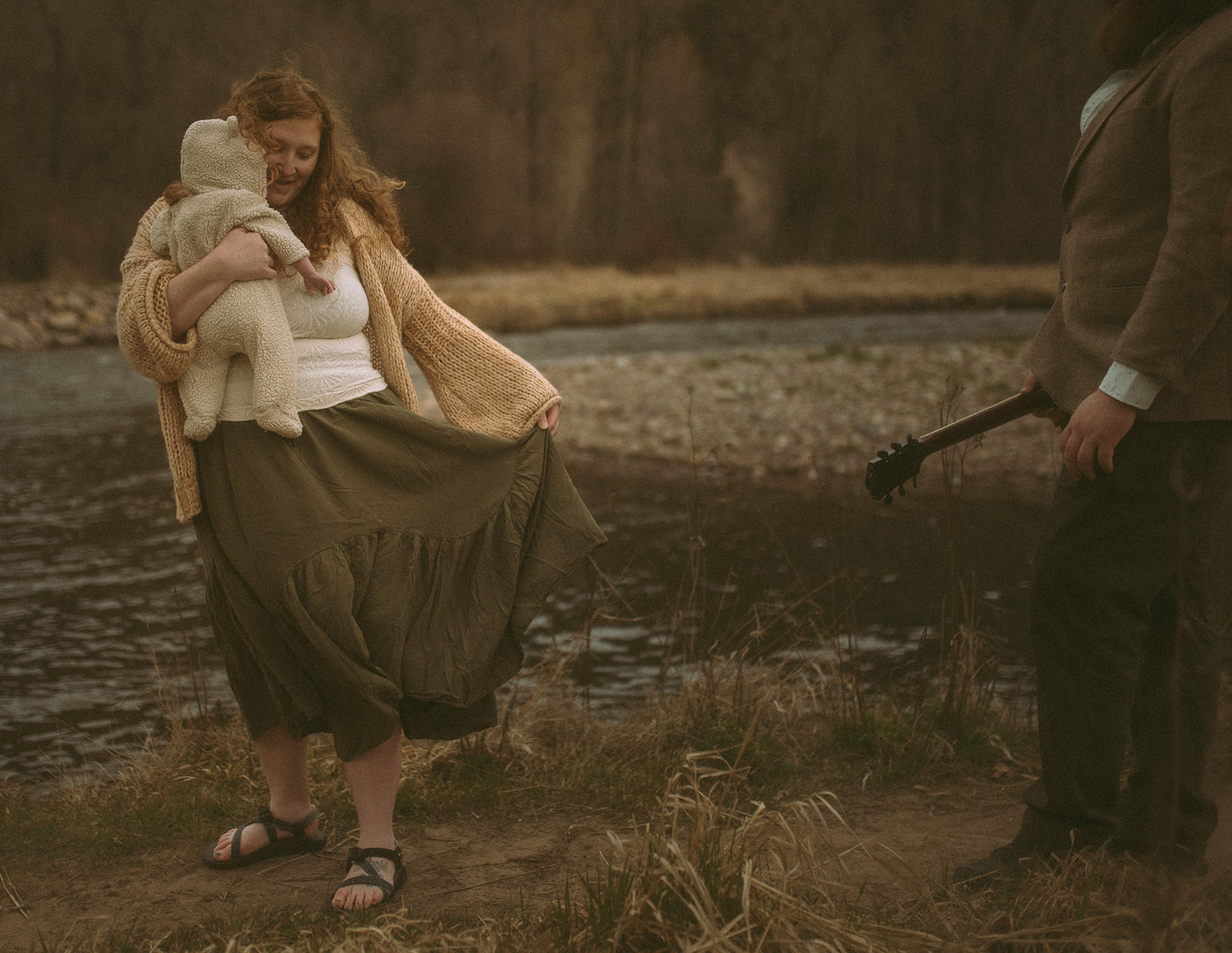 A happy mom dances by the river in a green skirt while holding her infant close to her cheek after some pelvic floor therapy in Hamilton, MT