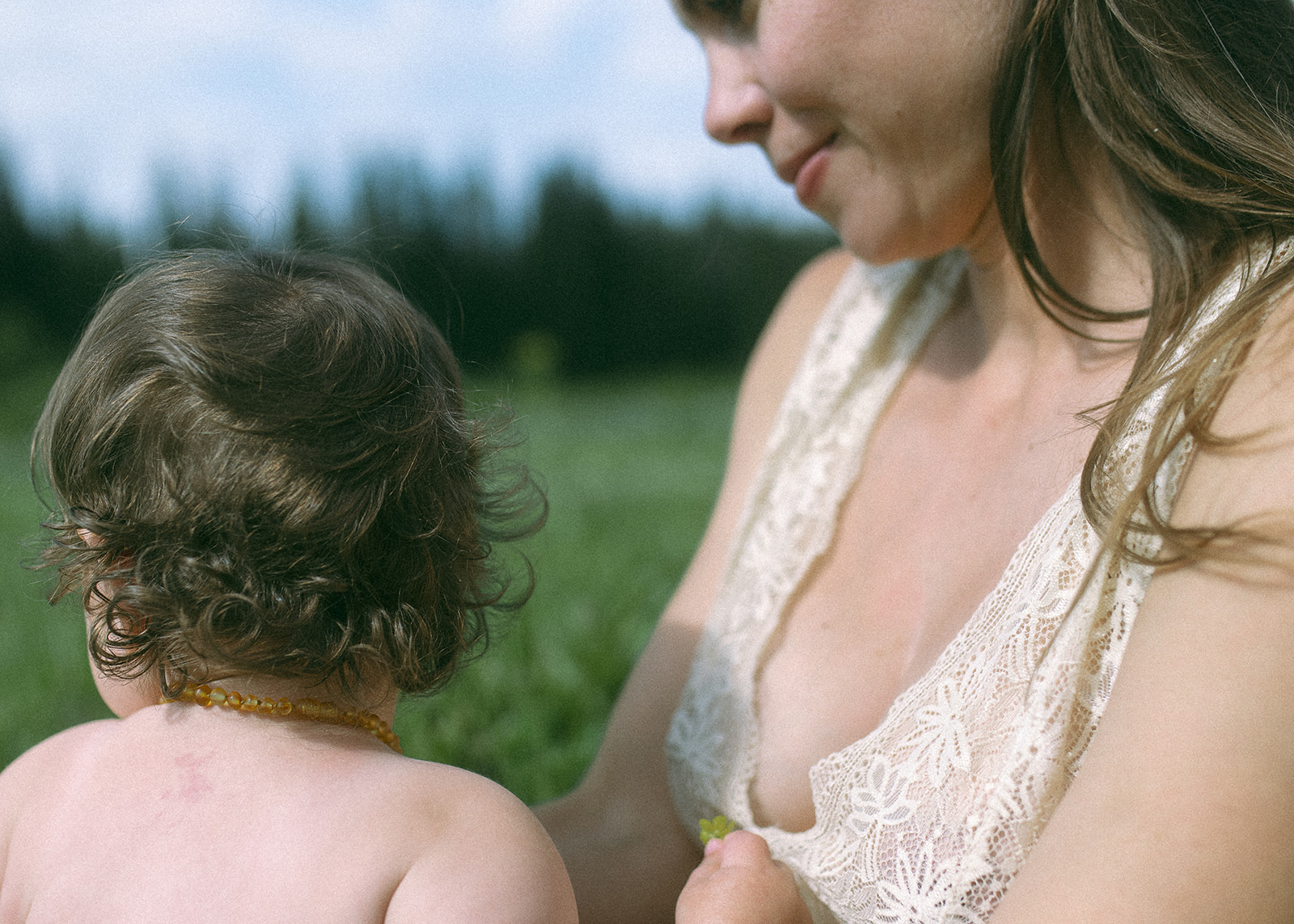 A smiling pregnant mother admires her infant in her lap as they sit in a pasture picking flowers