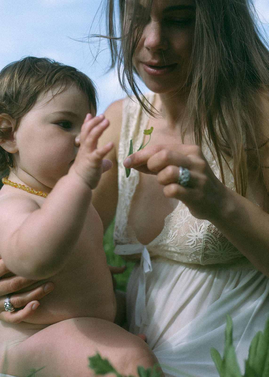A pregnant mother explores picking some small plants with her infant in a field in a white gown after some prenatal yoga in Hamilton, MT
