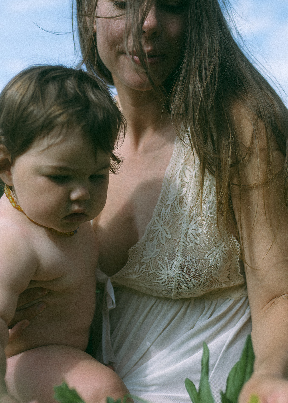 A mom in a white gown holds her infant while exploring some plants after some prenatal yoga in Hamilton, MT