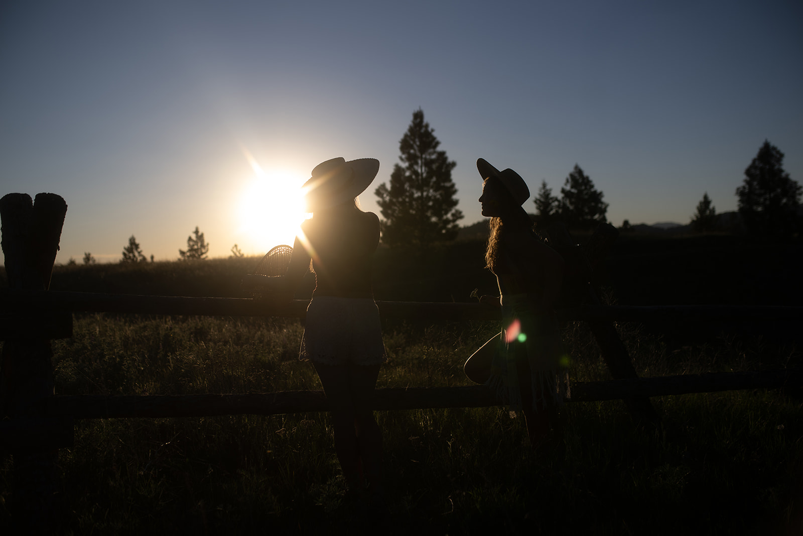 Two women lean on a wooden pasture fence in a field watching the sunset after visiting a private school in Hamilton, MT