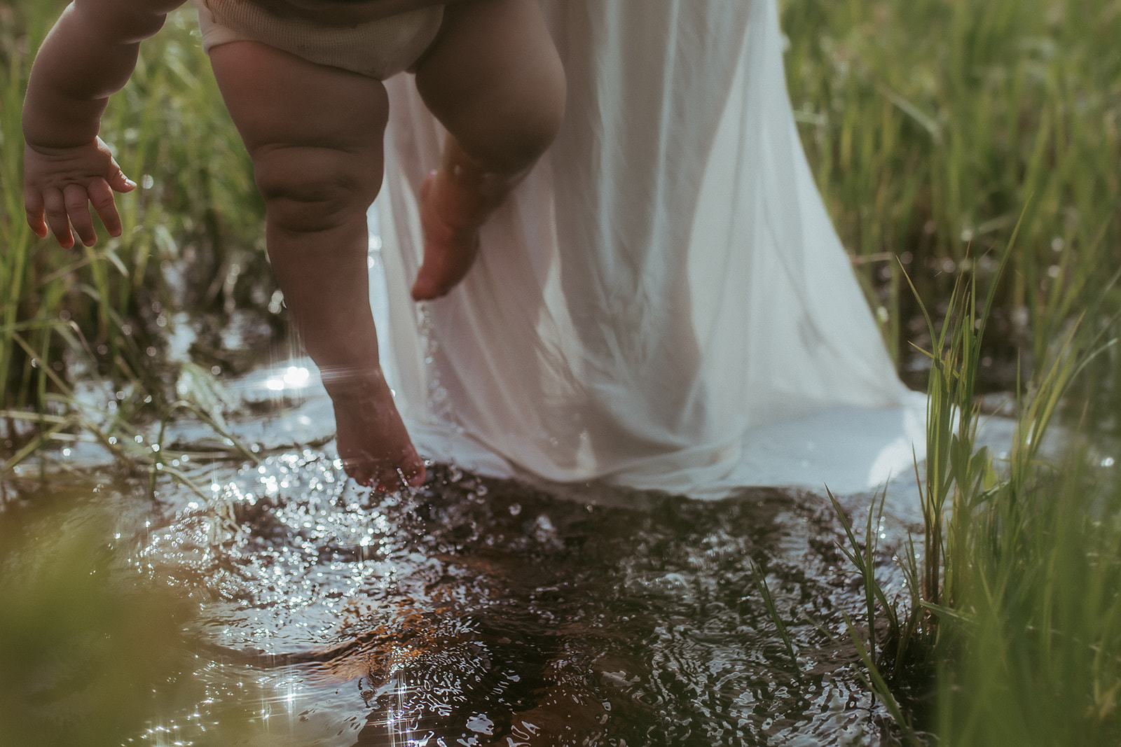 Details of a baby being dipped into a shallow creek by mom in a white dress after some swim lessons in Hamilton, MT