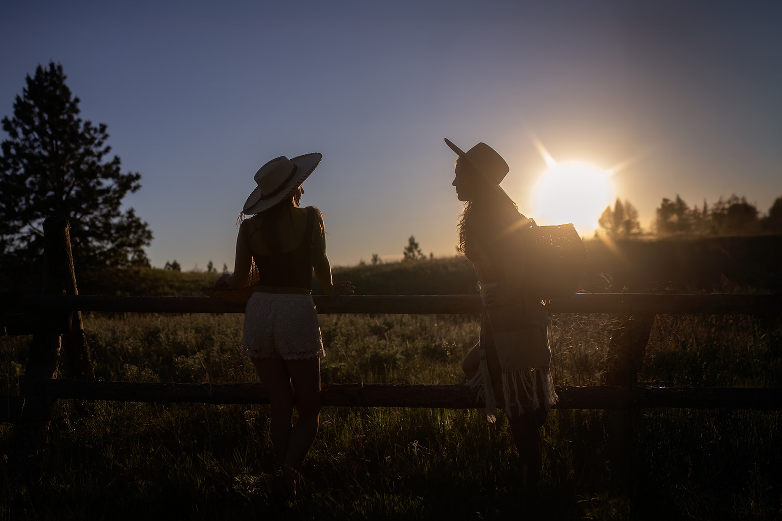 Silhouette of two women in large hats leaning on a pasture fence at sunset after an apple festival in Hamilton, MT