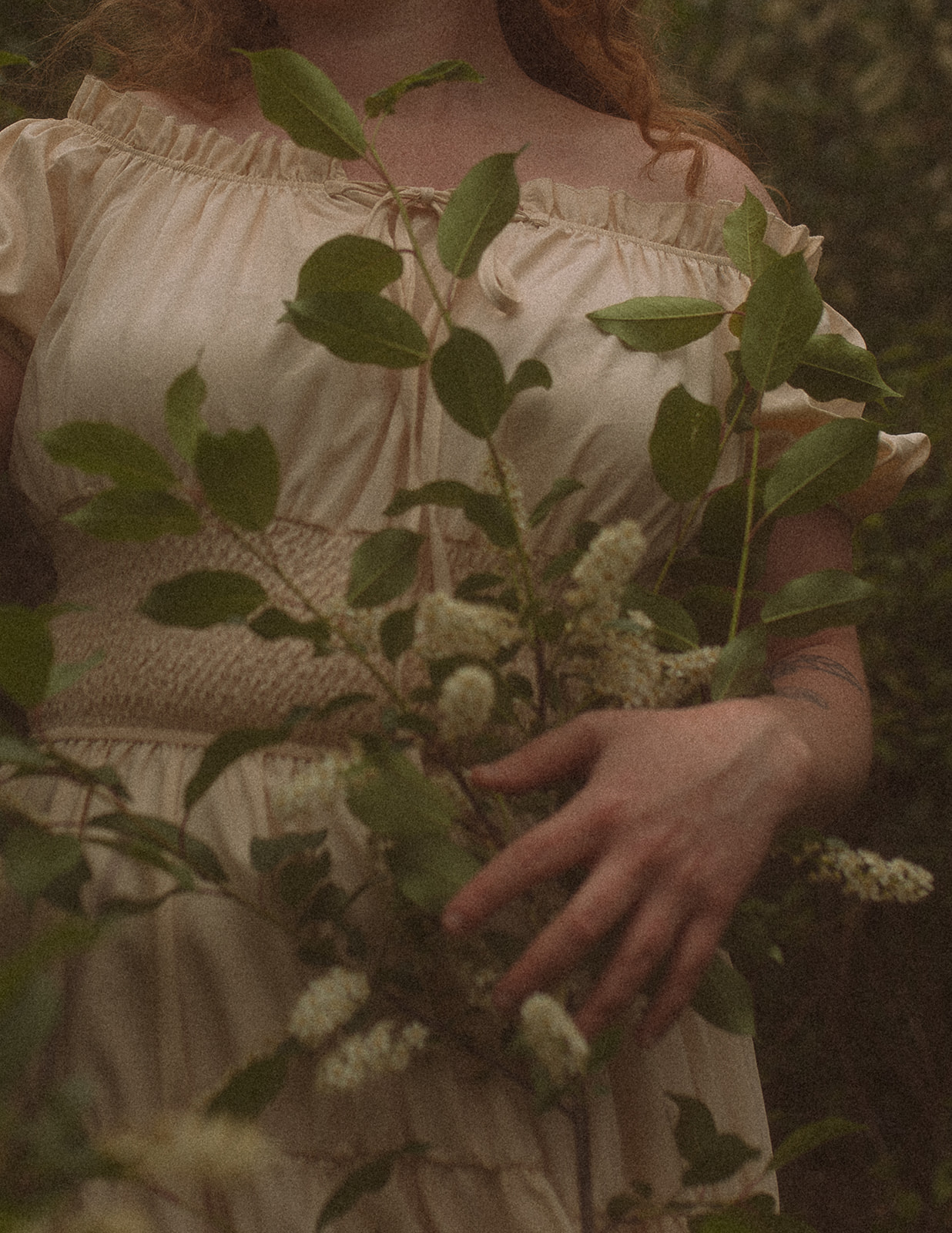Details of a woman in a white dress holding some white flowering sprigs in a forest