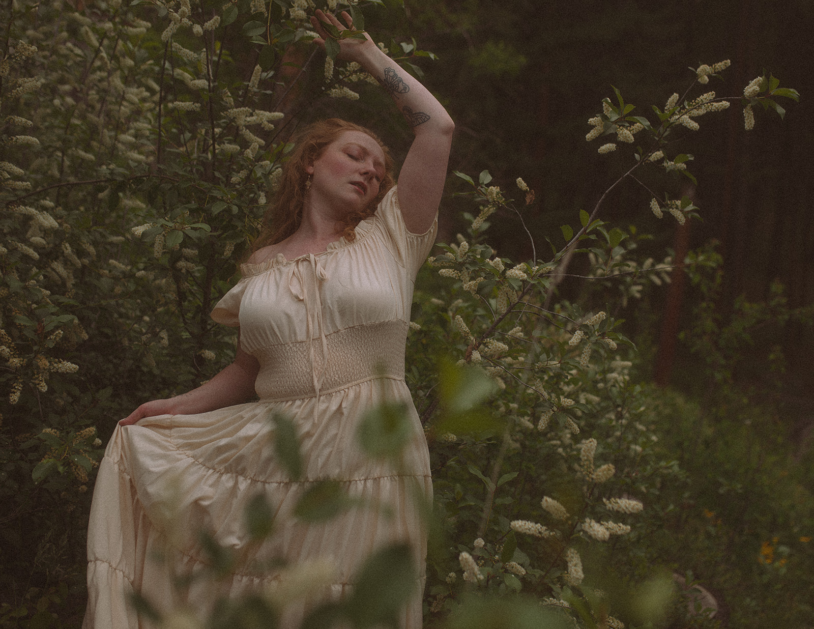 A woman in a white dress dances in a flowering bush with eyes closed before finding fall activities in Hamilton, MT