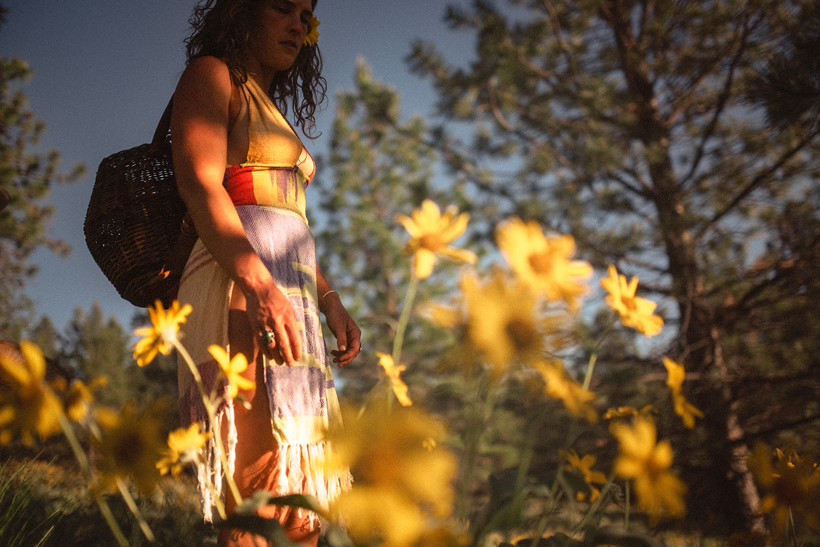 A woman in a colorful dress walks in a field of yellow wildflowers with a woven basket on her back