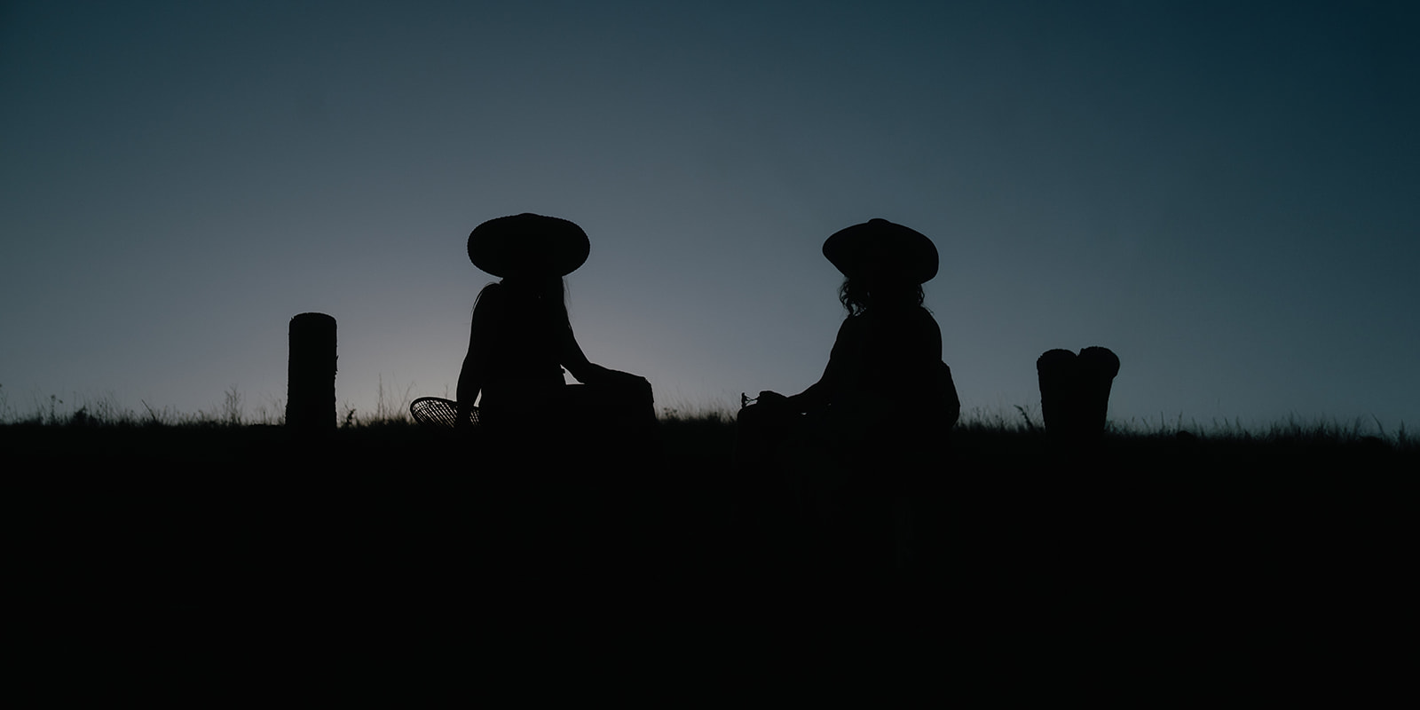 Silhouette of two women sitting in a meadow at sunset in large hats after visiting a pumpkin patch in Hamilton, MT