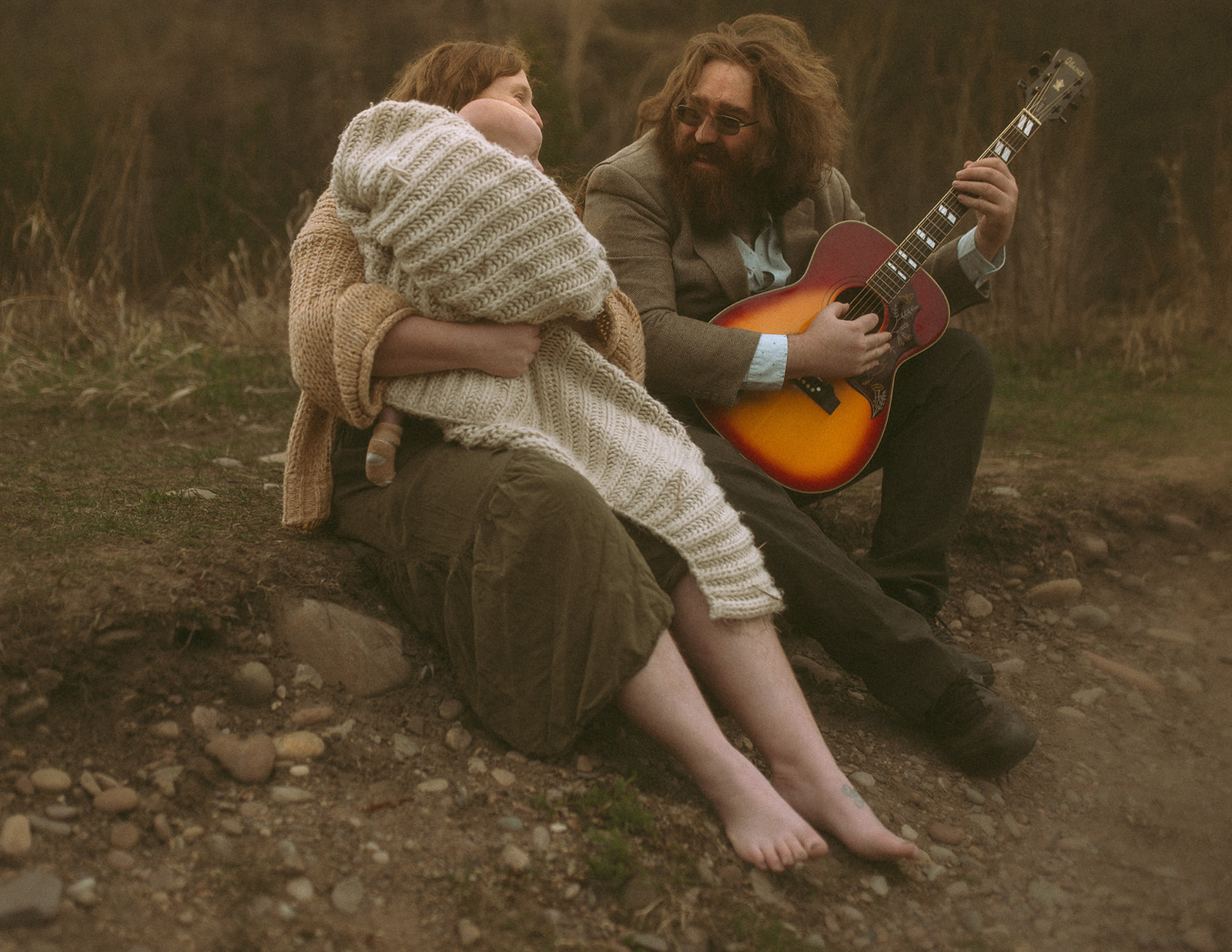 A happy family sit on a trail playing guitar while wrapped in blankets