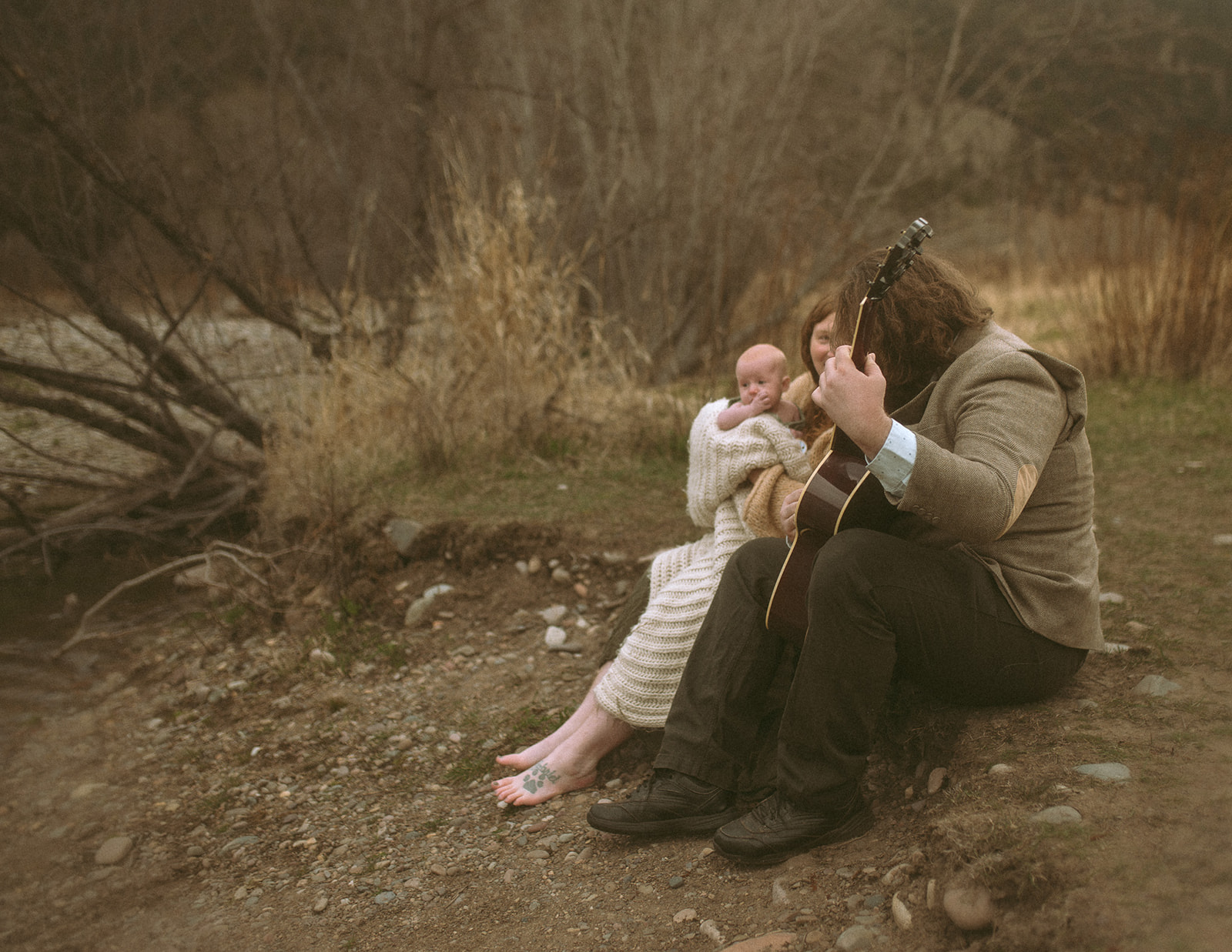 A new dad sits on a trail playing guitar to his wife and newborn daughter in her arms after visiting Missoula Fall Events