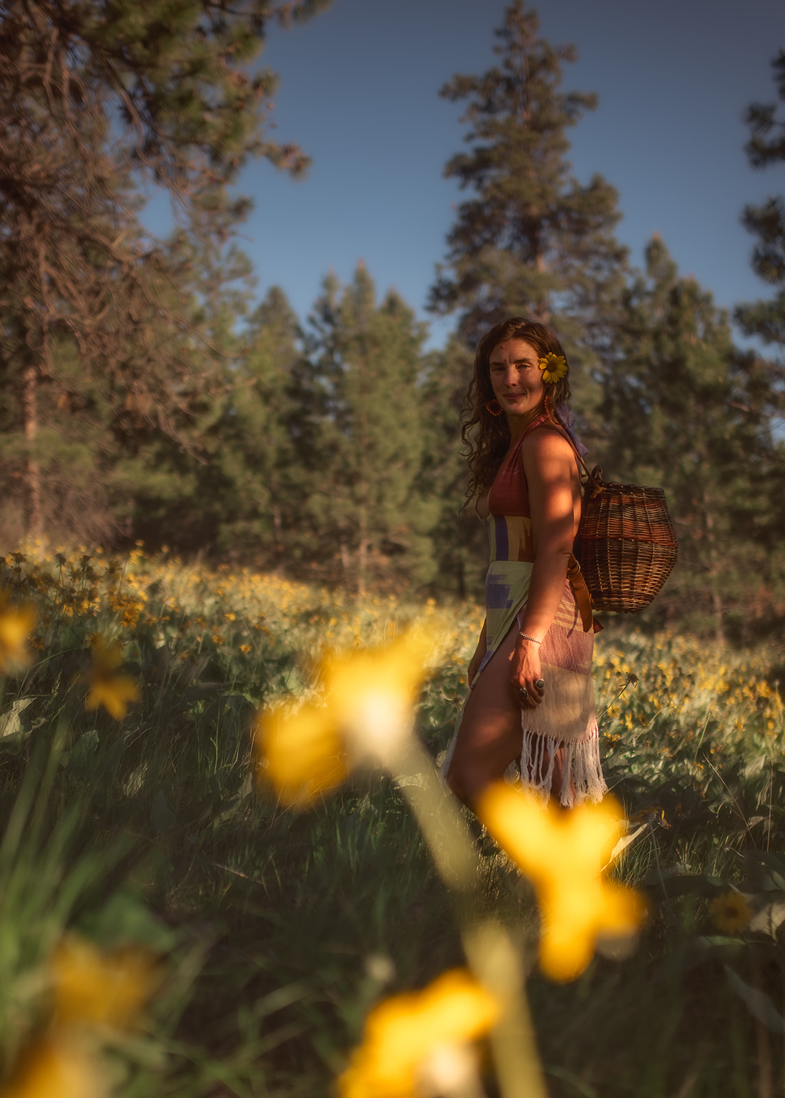 A woman walks with a wicker basket on her back through wildflowers at sunset before visiting a pumpkin patch in Missoula