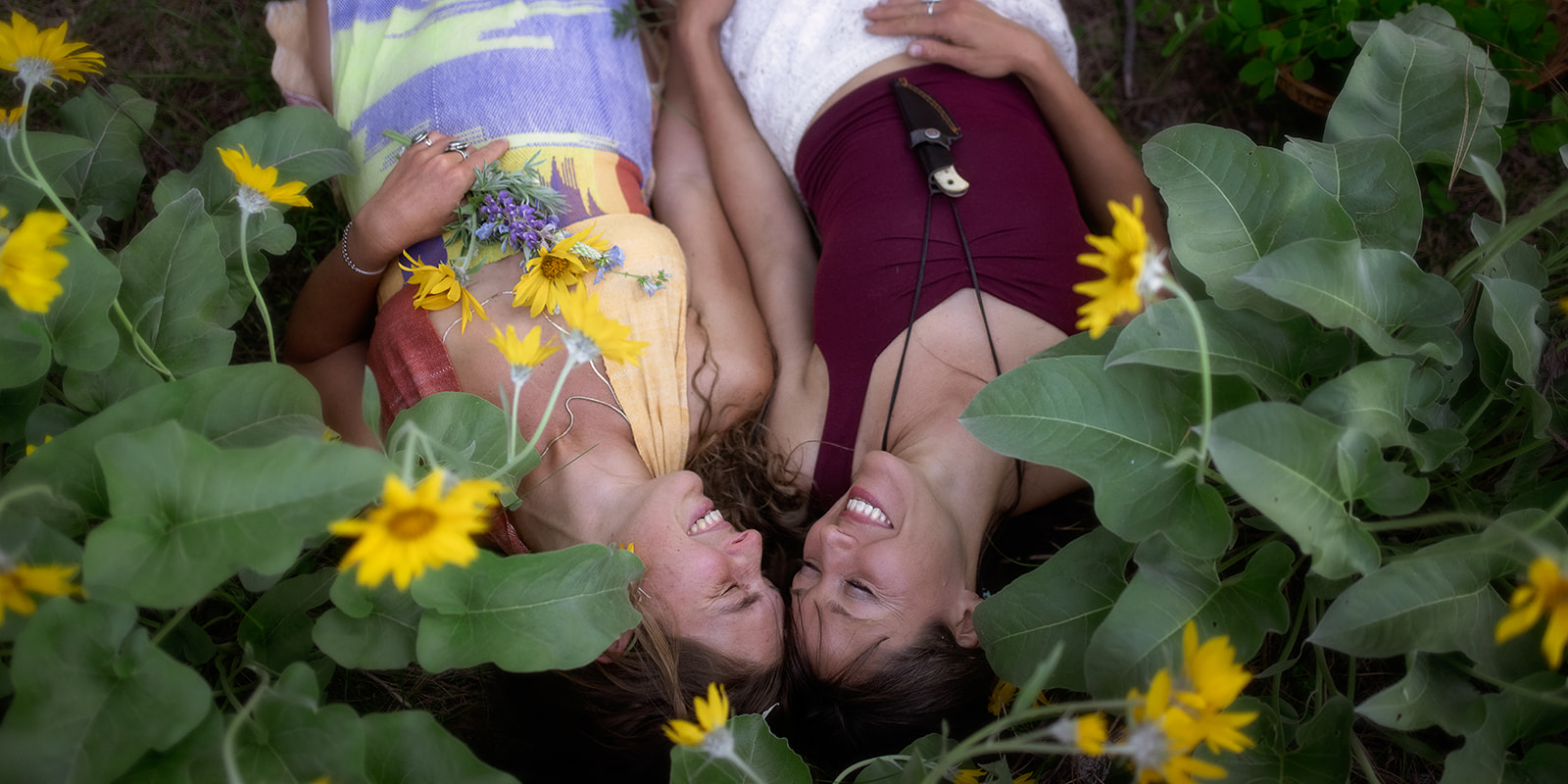 A happy couple snuggle touching heads while laying in a patch of wildflowers before visiting a pumpkin patch in Missoula