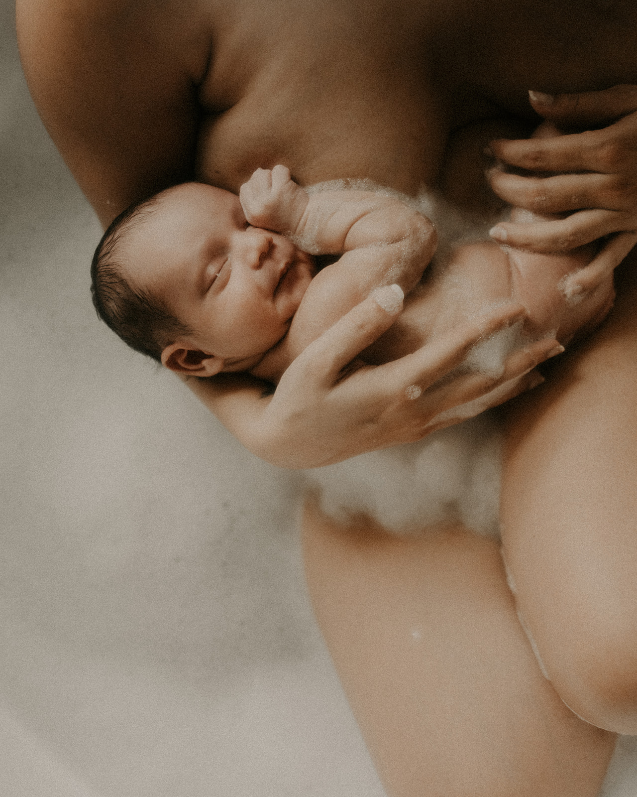 A newborn baby snuggle against mom's chest in a bathtub