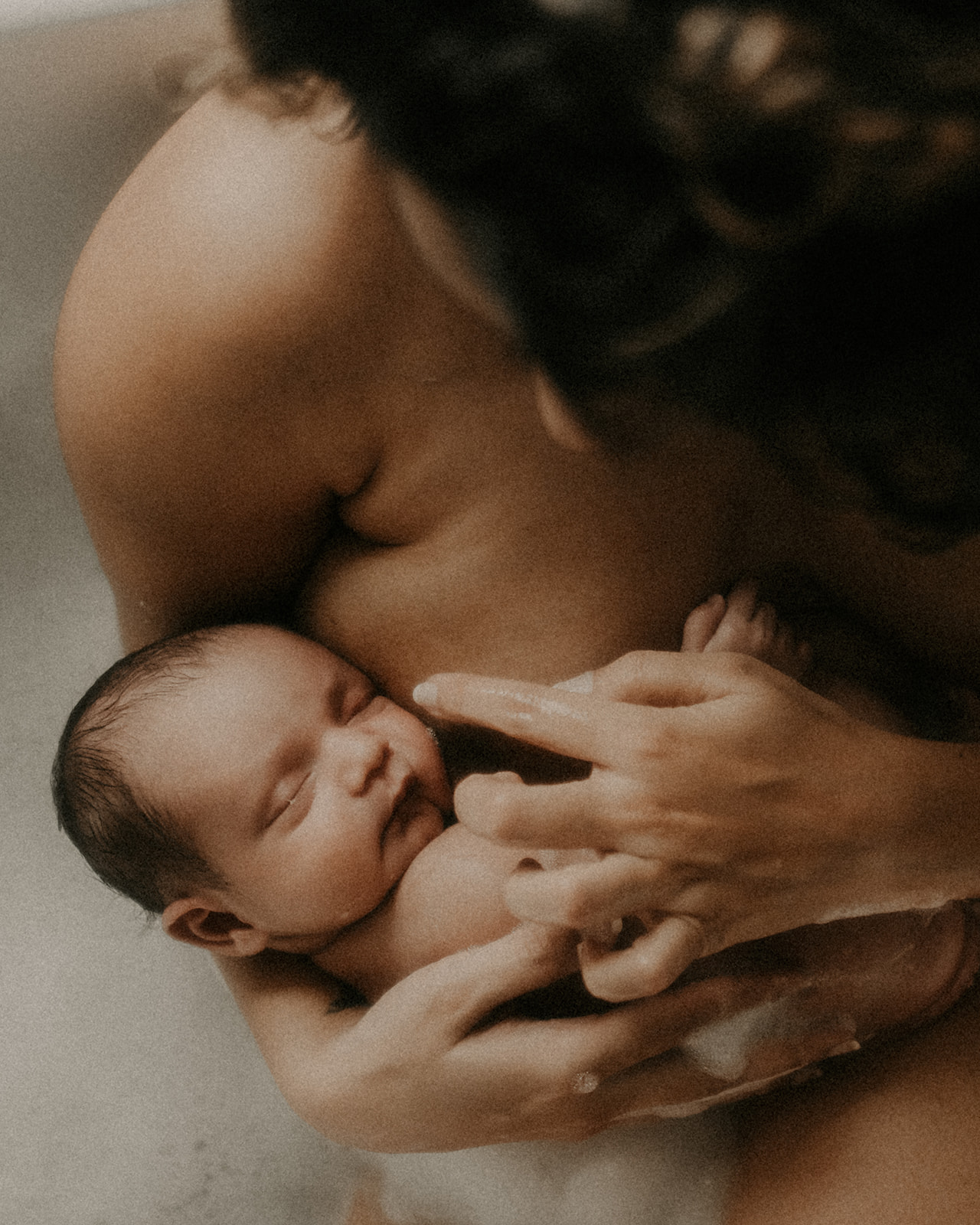 A look down to a newborn baby sleeping in mom's arms against her chest