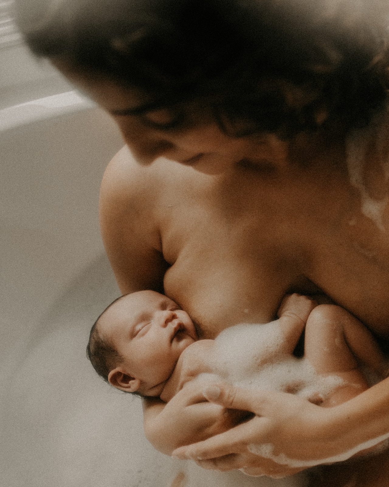 A new mother sits in a bathtub cradling her newborn against her chest thanks to Roots Birth Center Missoula