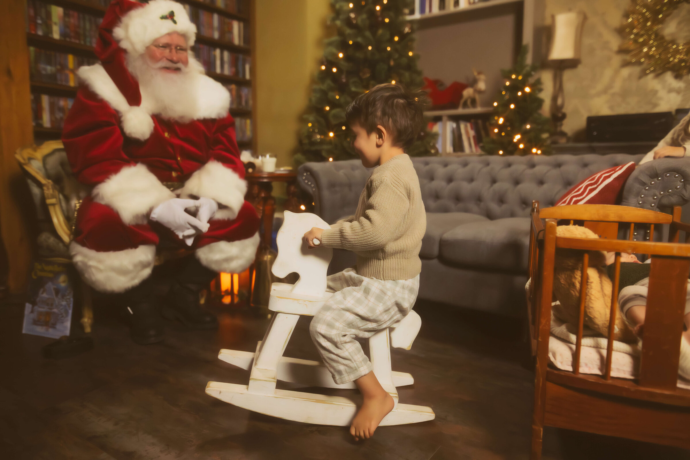 A toddler boy rides a wooden rocking horse in a living room as Santa watches before watching the missoula tree lighting