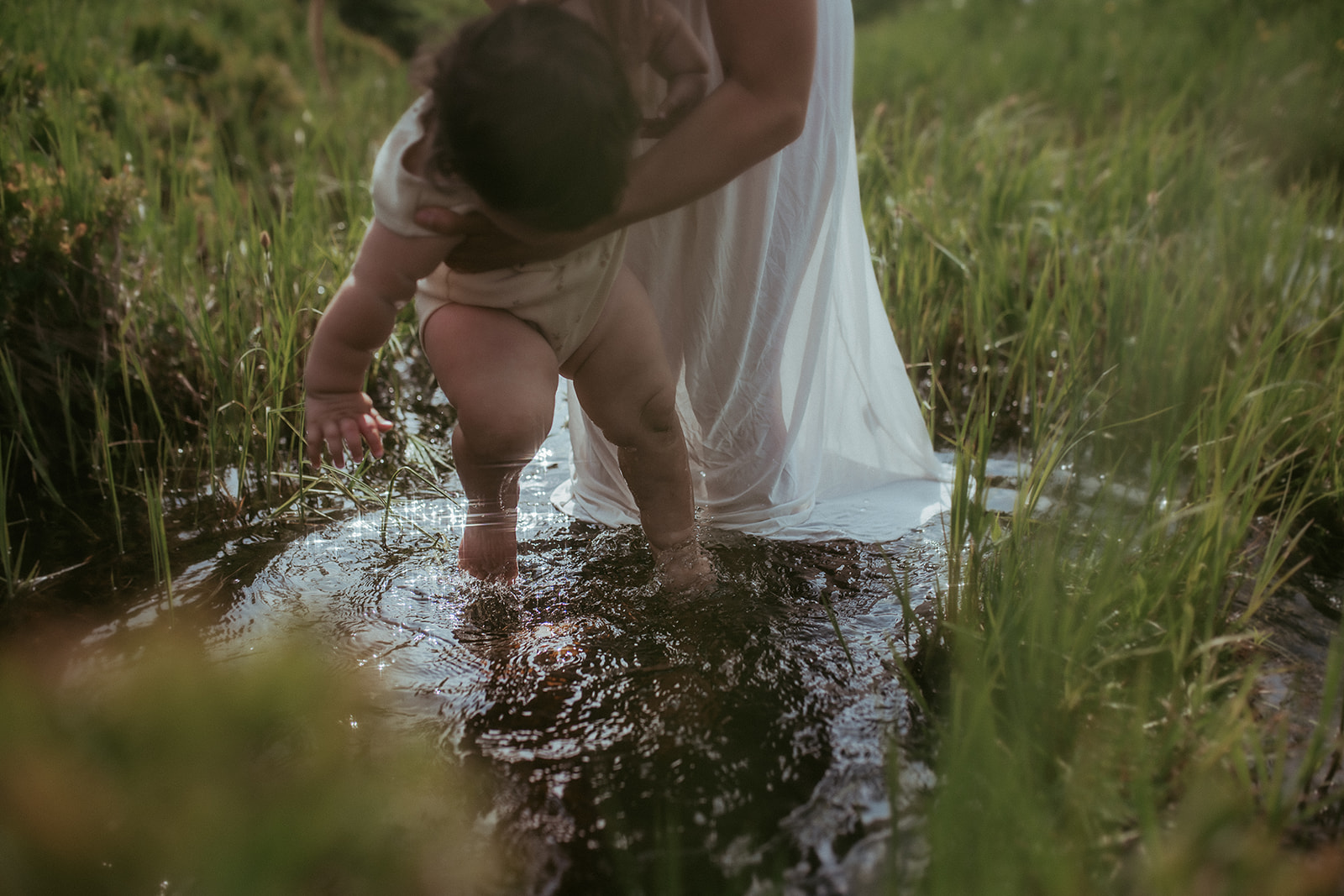 a young toddler's feet are dipped in the water by mom in a white dress at one of the parks in Hamilton, MT