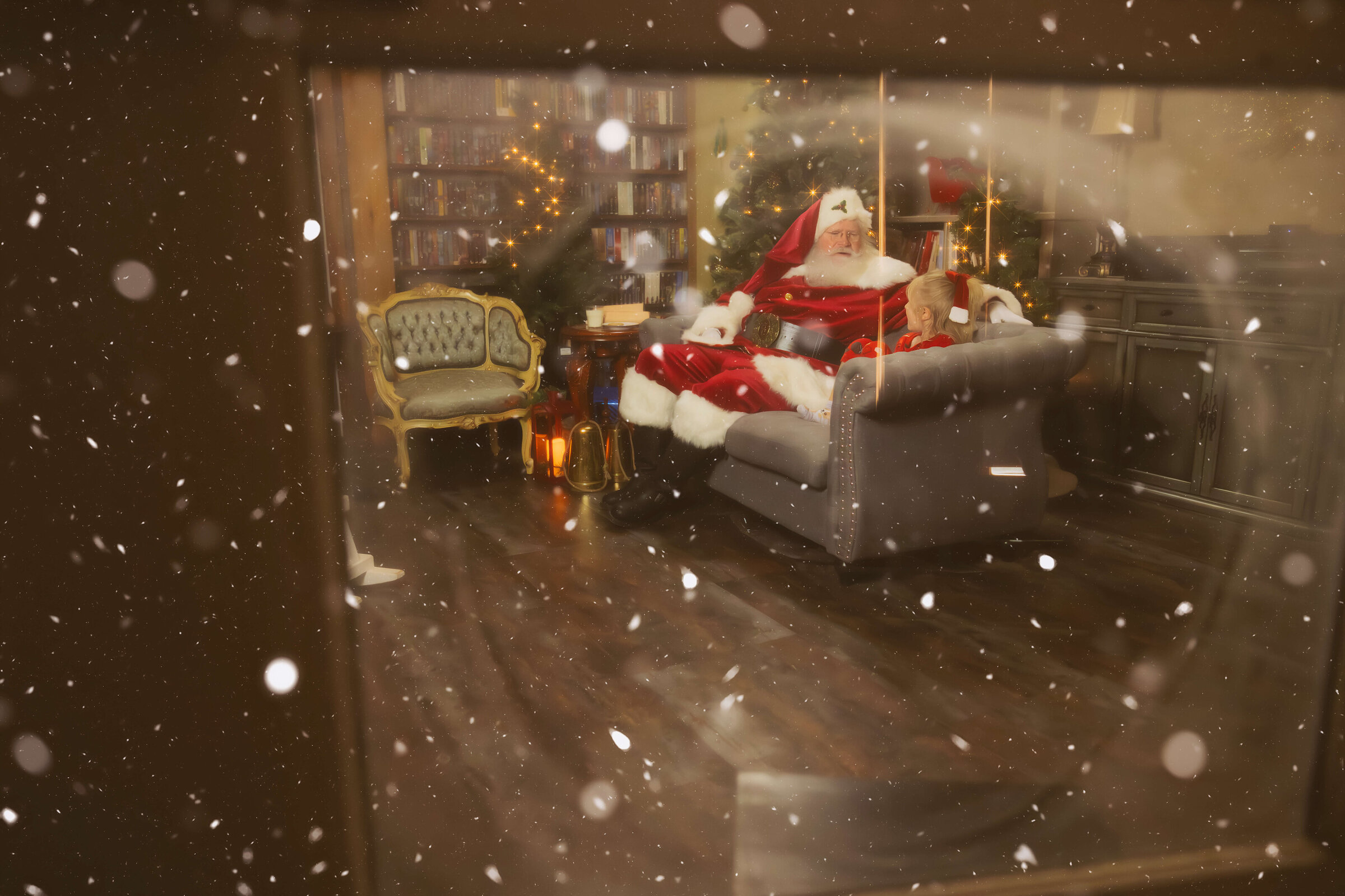 A young girl in red pajamas laughs while chatting with santa seen through a snow covered window