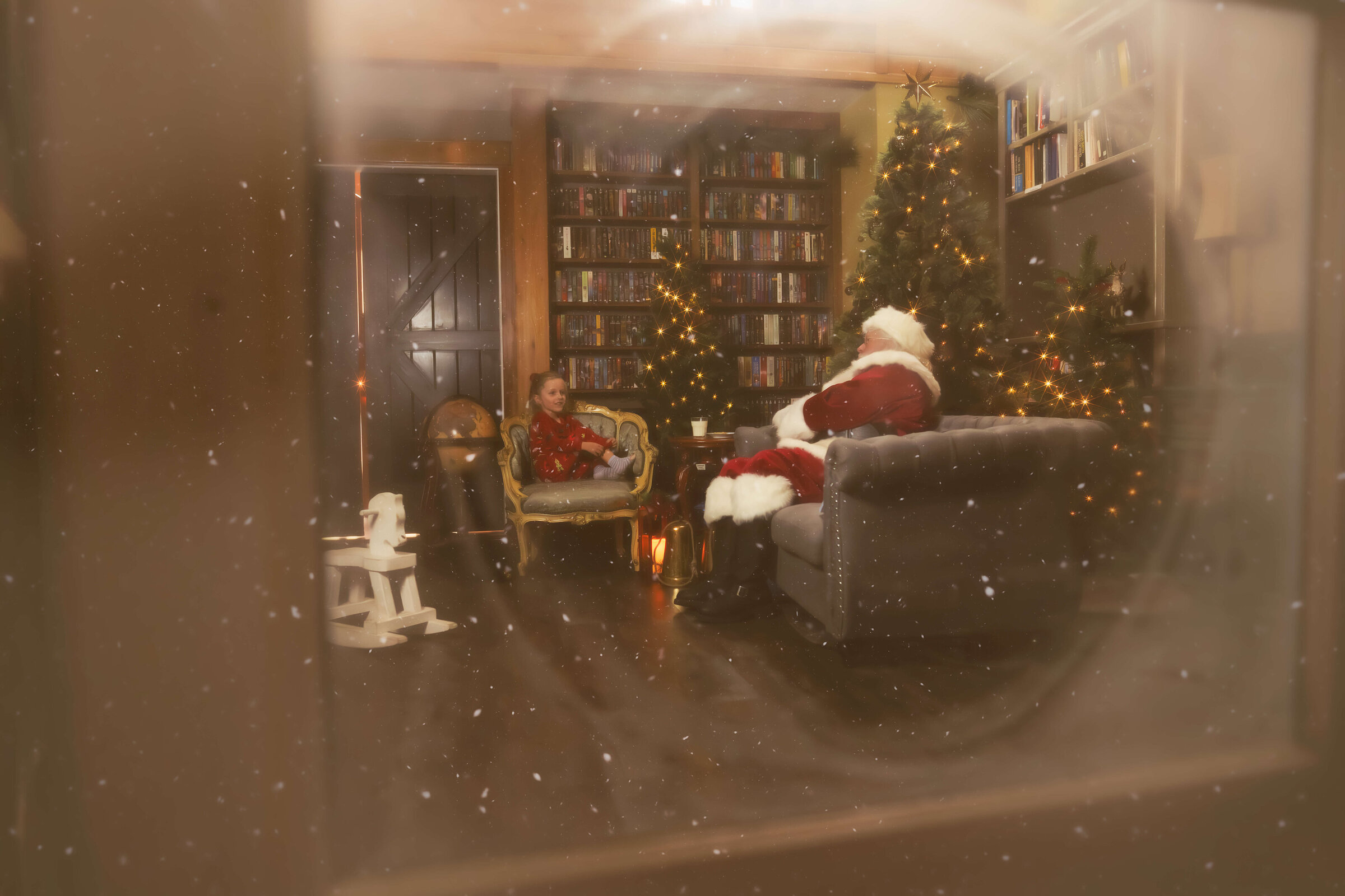 A peek through a window of a young girl in red pajamas in a christmas decorated living room chatting with a santa in hamilton, mt on a couch