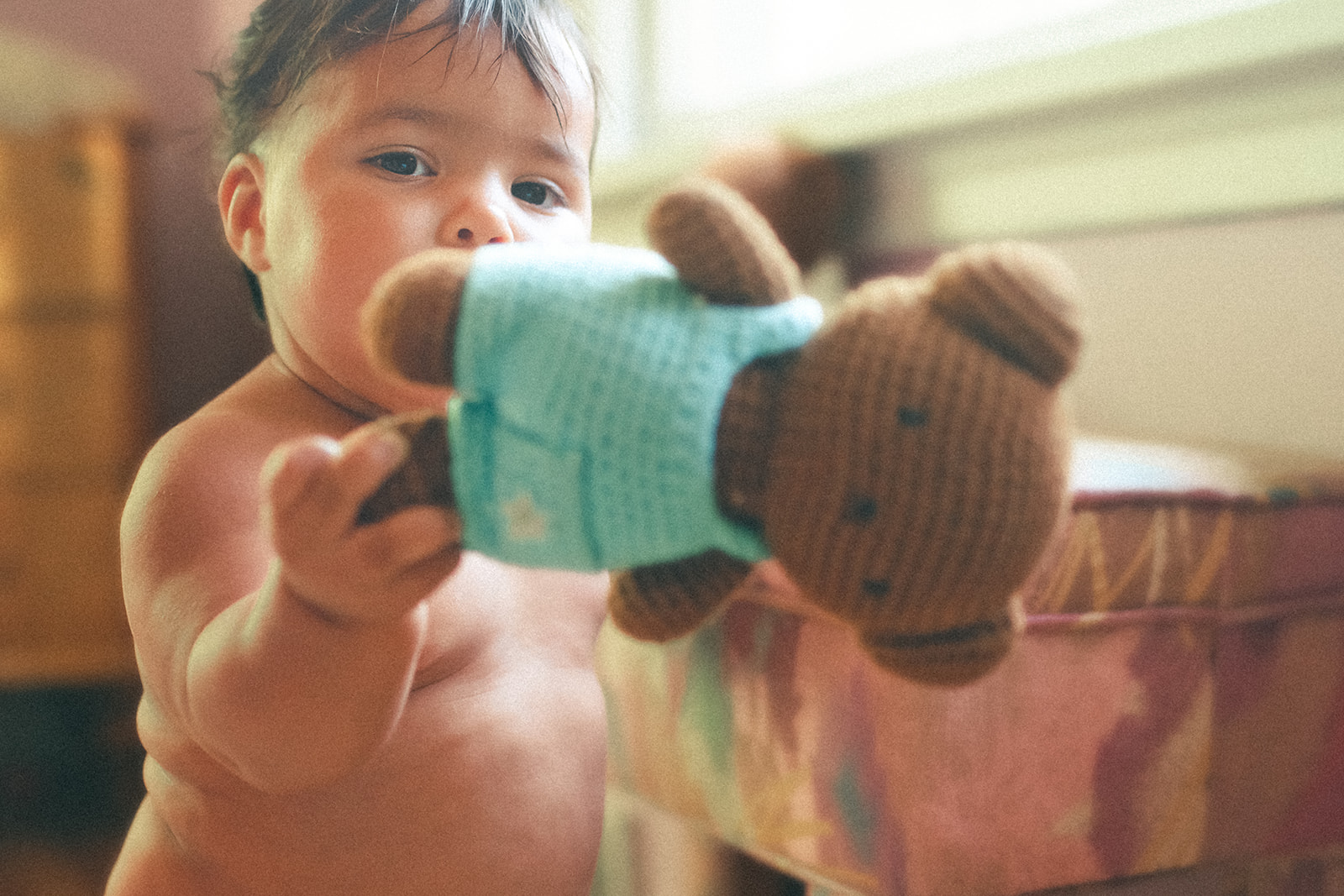A shirtless baby plays with a teddy bear under a window after visiting daycares in Polson, MT