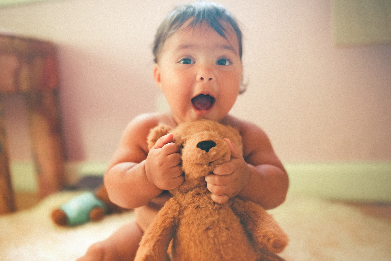 A toddler sits in a nursery playing with a stuffed teddy bear with a big smile after visiting daycares in Polson, MT