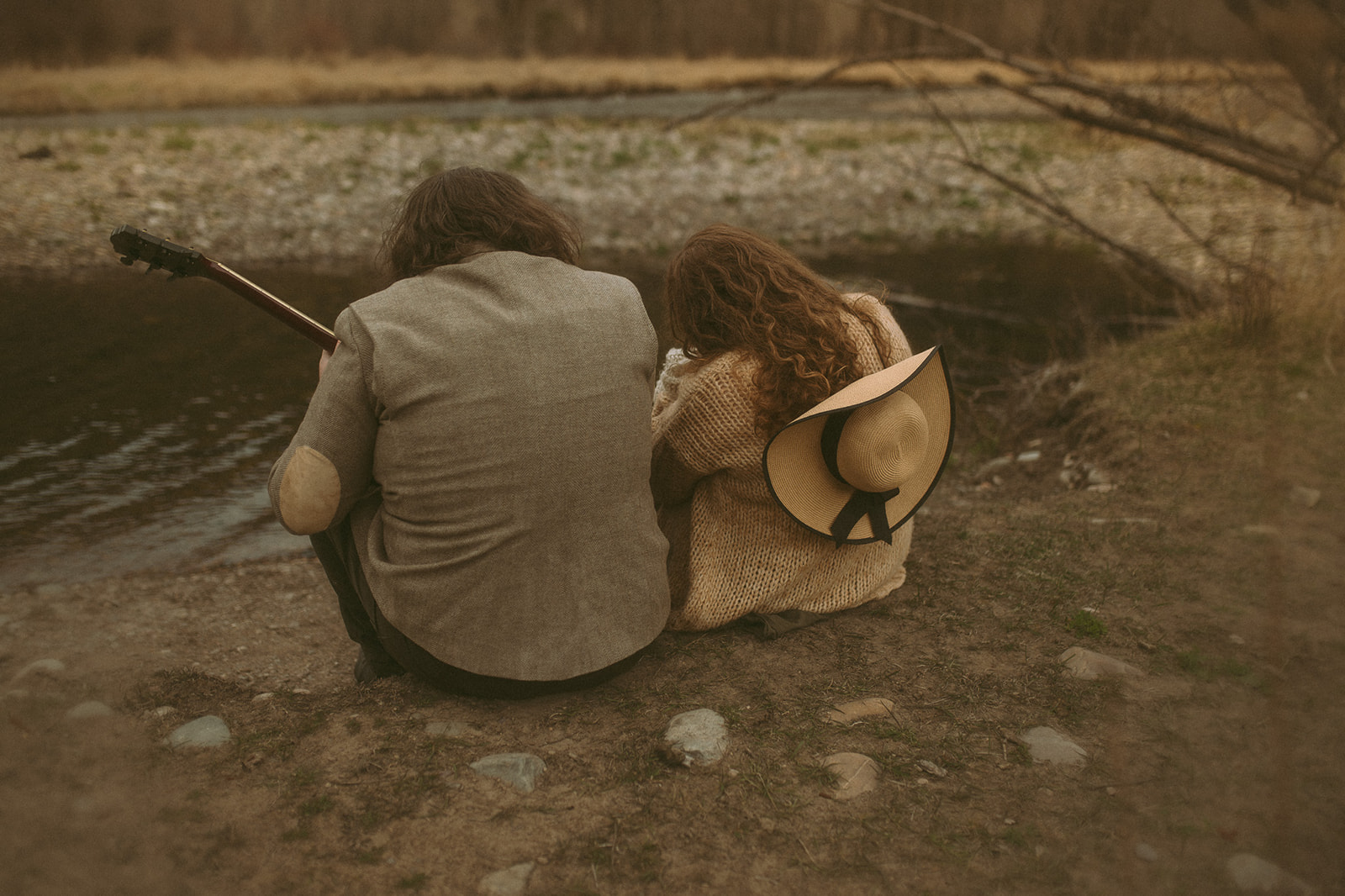 New parents sit on the edge of a river with their newborn and a guitar during some Hamilton, MT activities