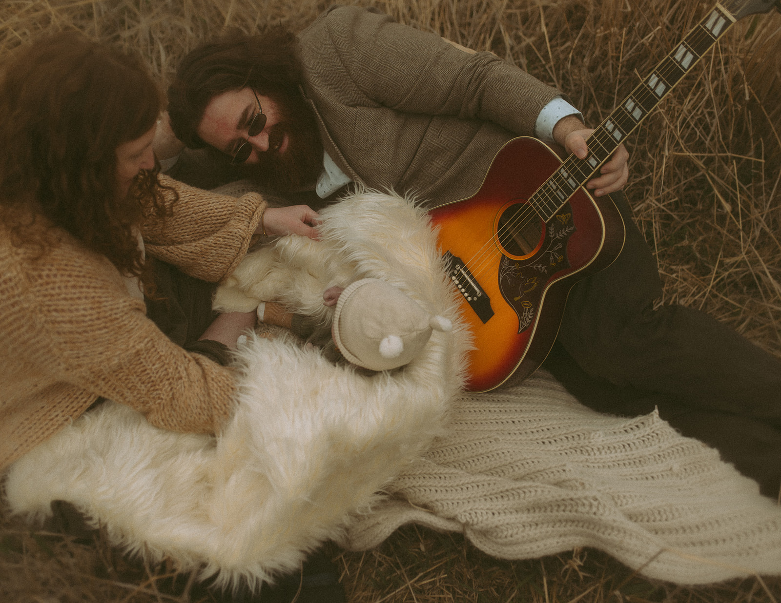A mom and dad snuggle on a picnic blanket with their newborn in a fur blanket with a guitar during some Hamilton, MT activities