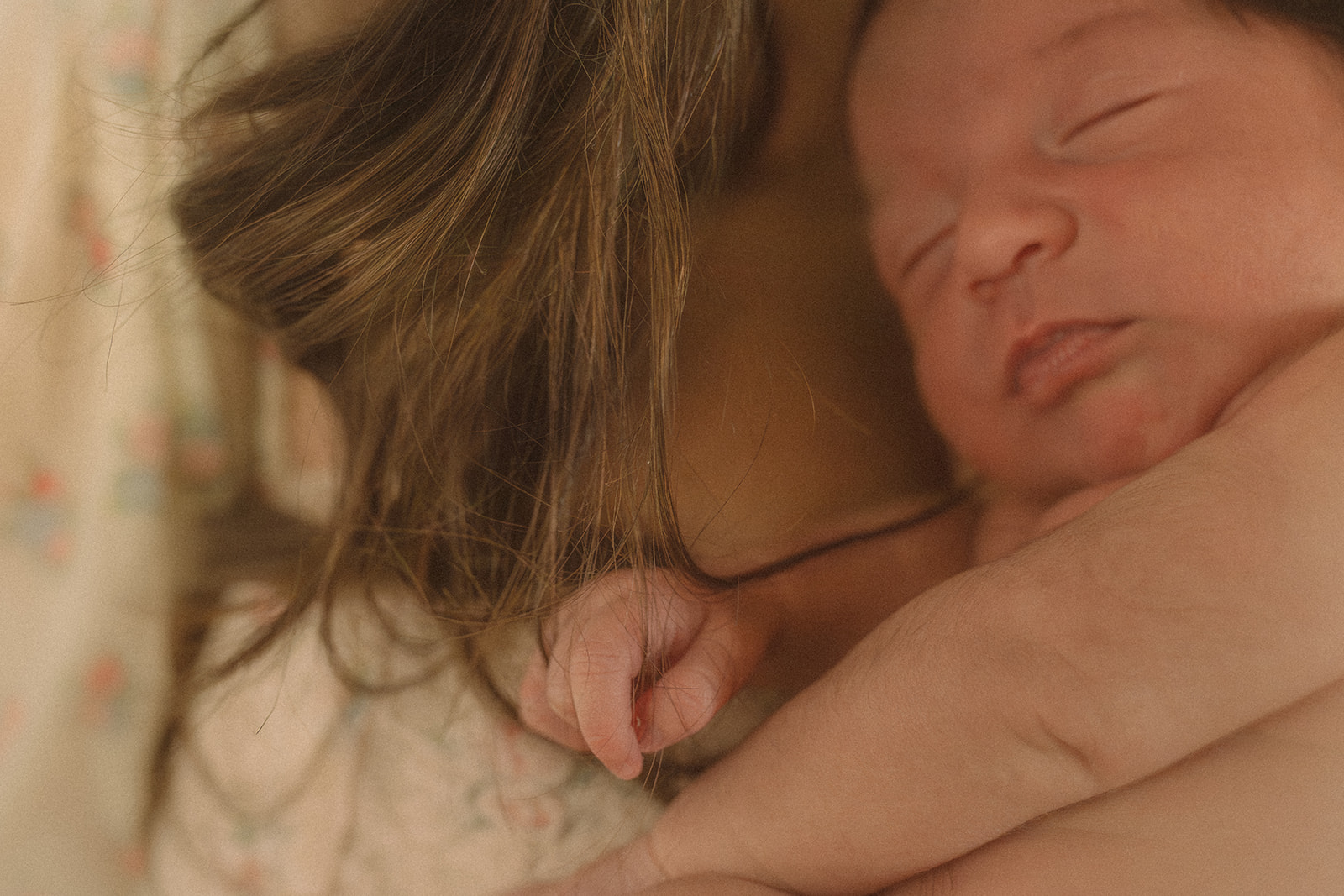 Details of a sleeping newborn baby's hand gripping mom's hair