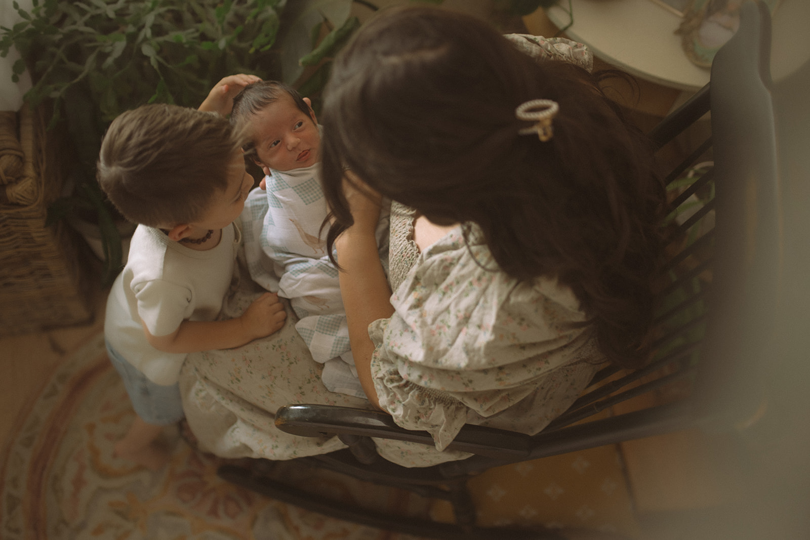 A look down at a newborn laying in mom's lap looking up to her as big brother pets his head