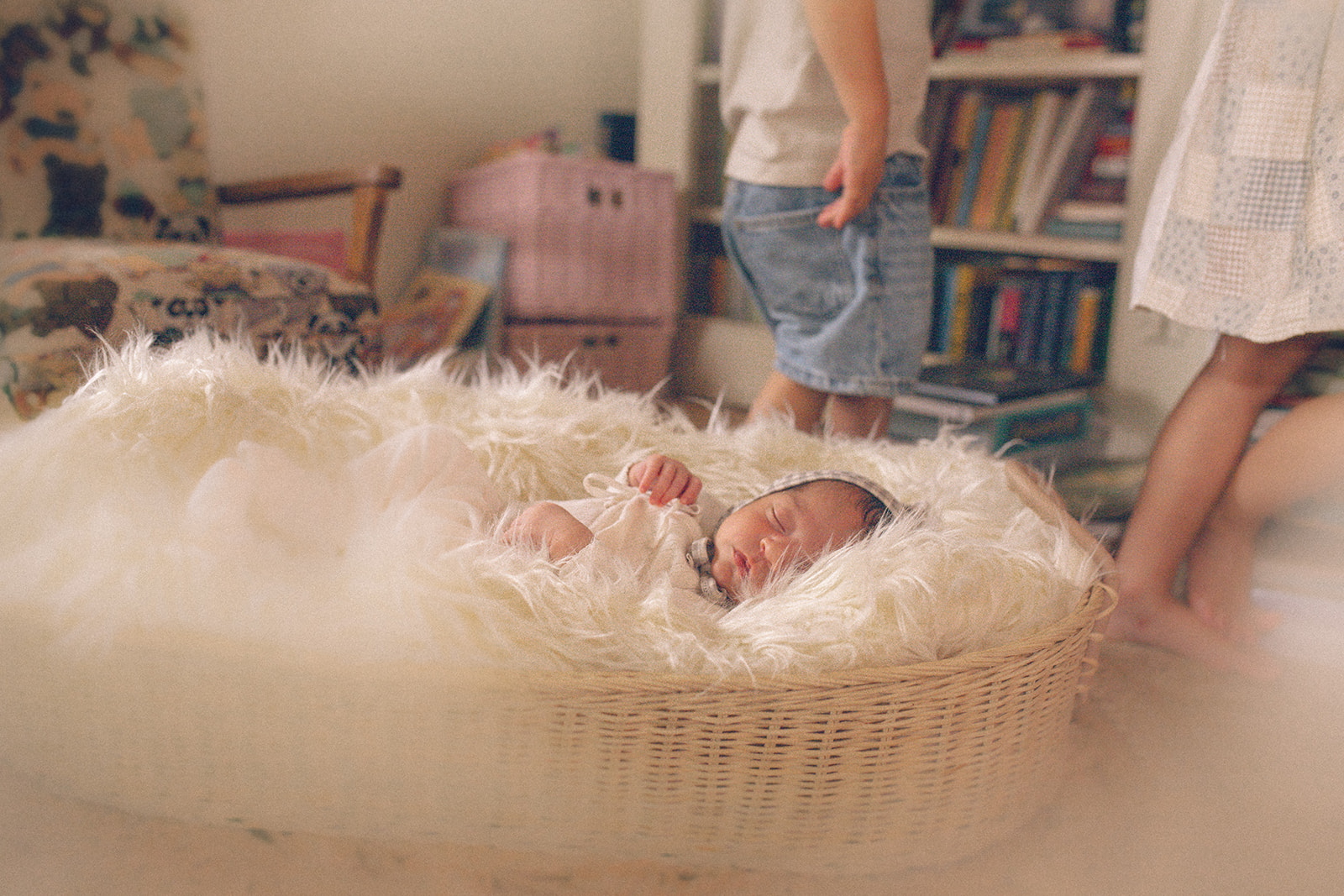 A newborn abby sleeps in a woven basket as big siblings walk around the nursery after visiting Briars Baby Boutique