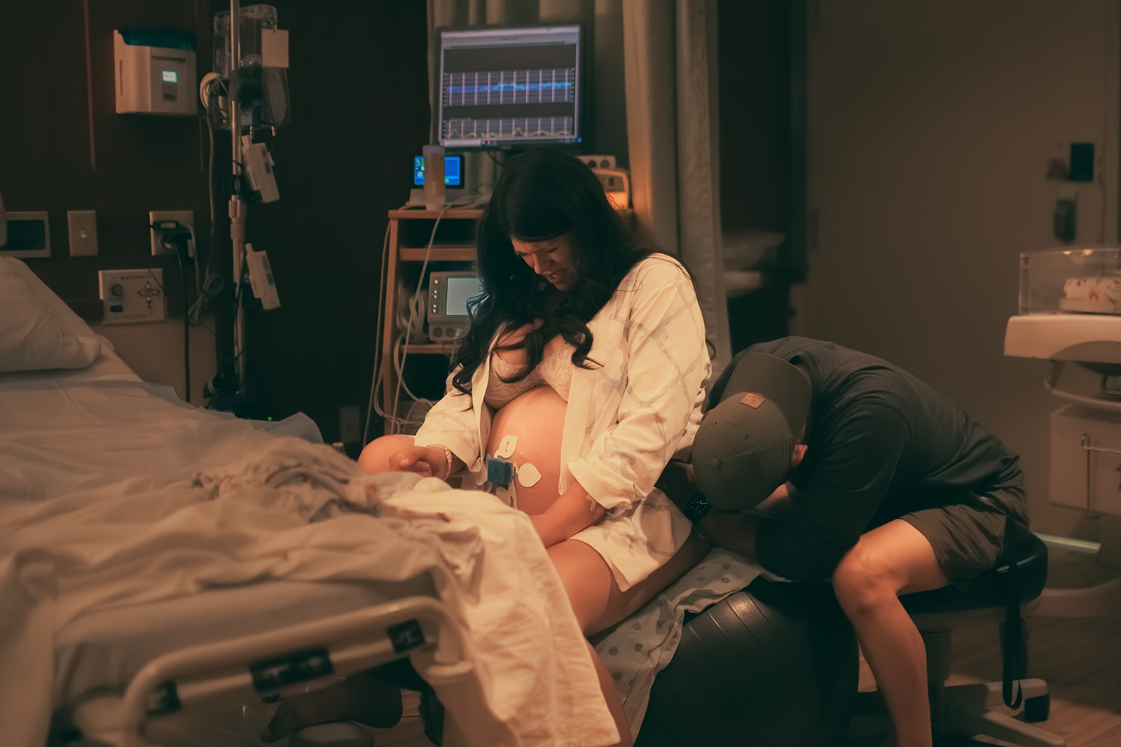 A mom to be in labor sits on a workout ball as her husband helps support as guided by midwives in Kalispell, MT