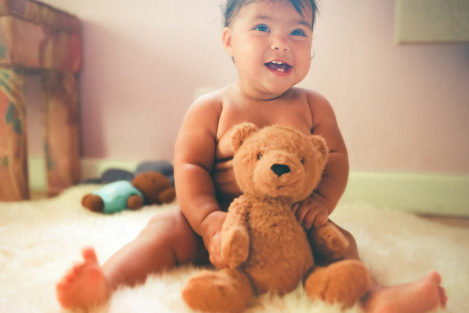 A happy baby sits in a pink room playing with a brown teddy bear before visiting preschools in polson mt