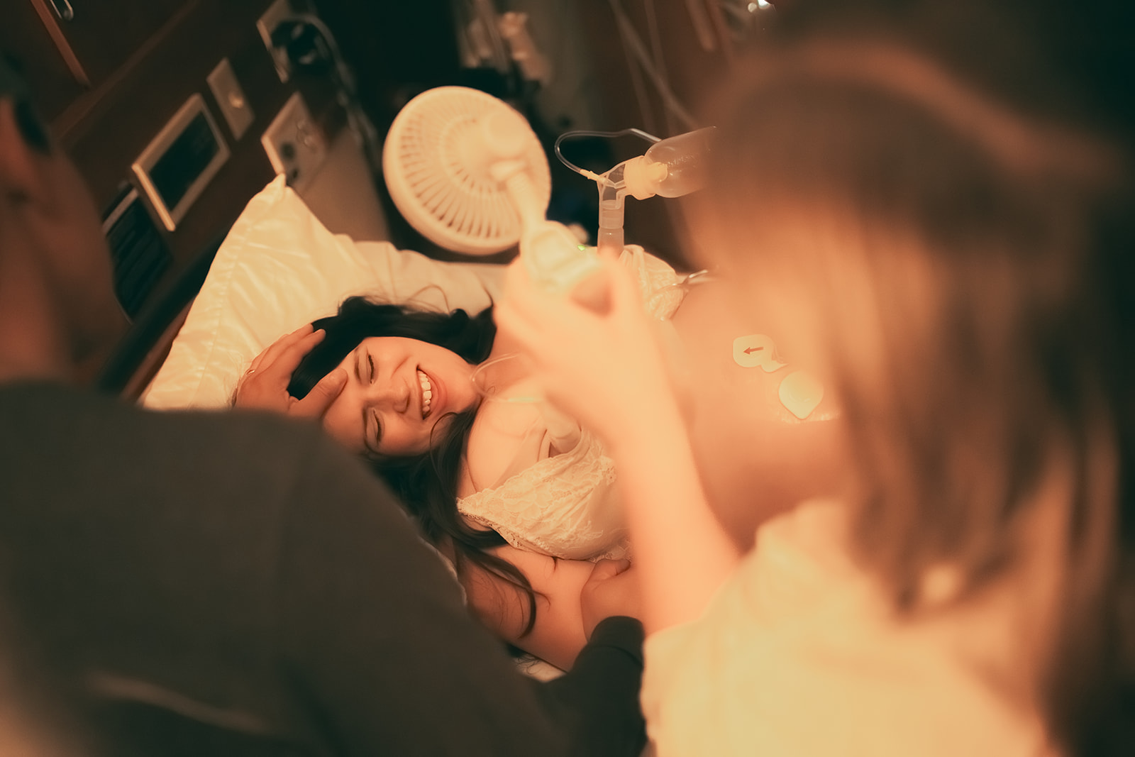 A smiling mother lays on a bed during delivery with support from Heart and Hands Midwifery