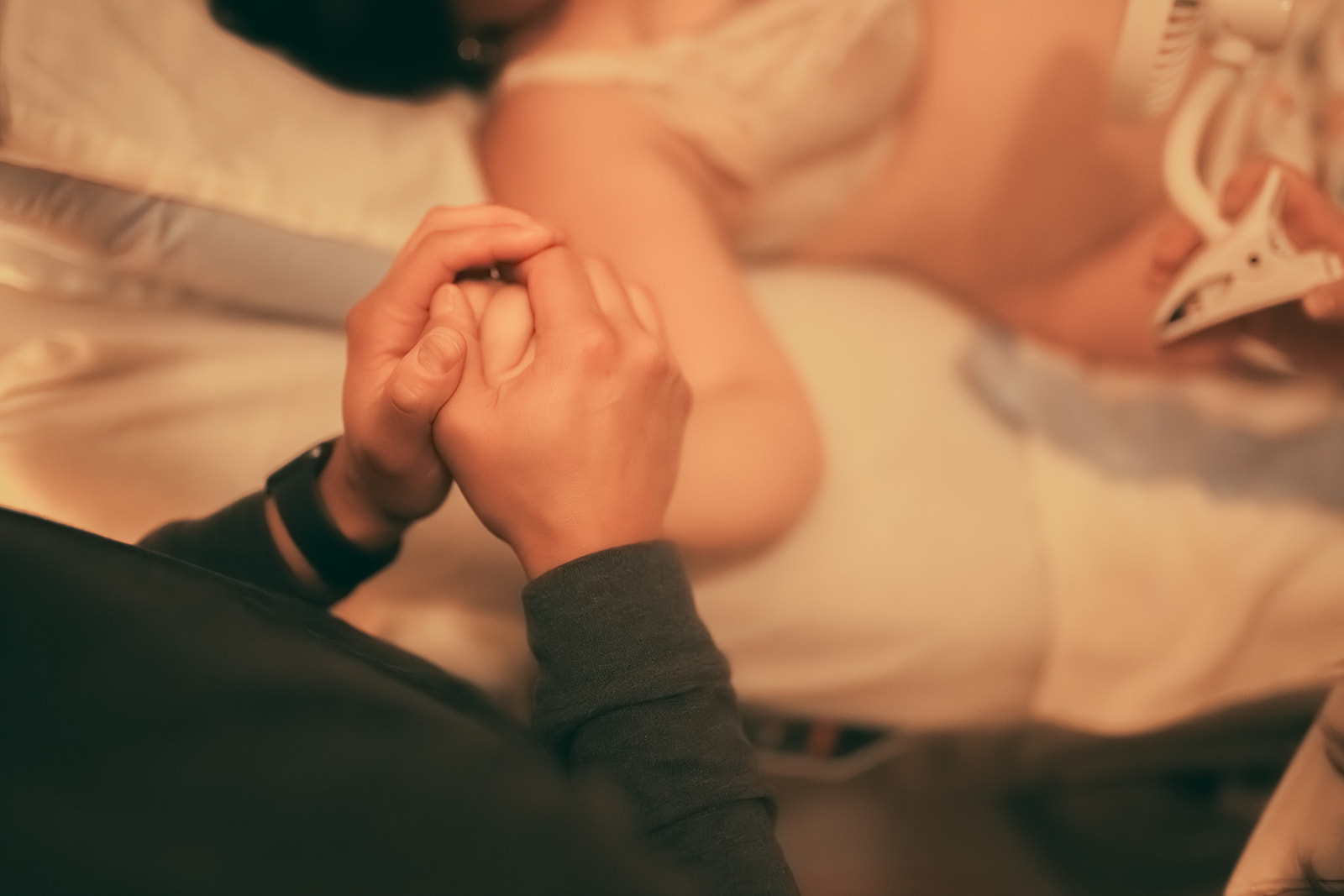 Details of a man holding his partner's hand as she gives birth with Heart and Hands Midwifery