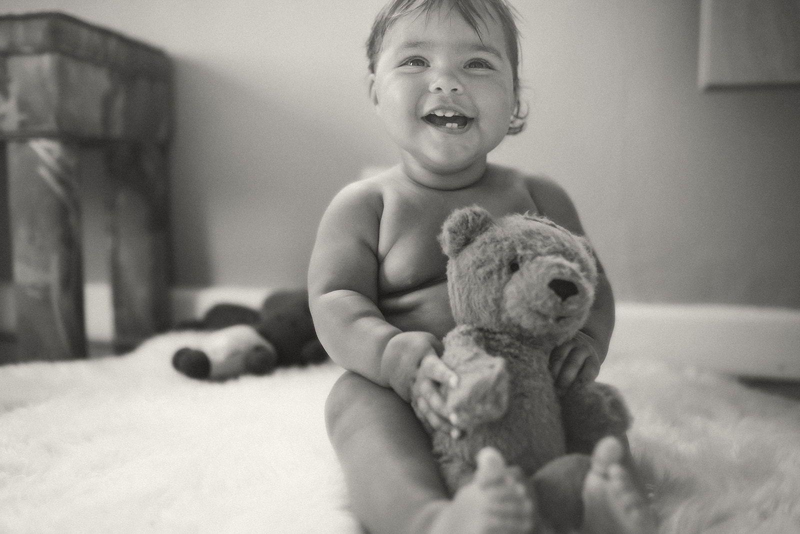 A happy baby plays with a soft teddy on the floor in black and white after visiting daycares in Kalispell, MT