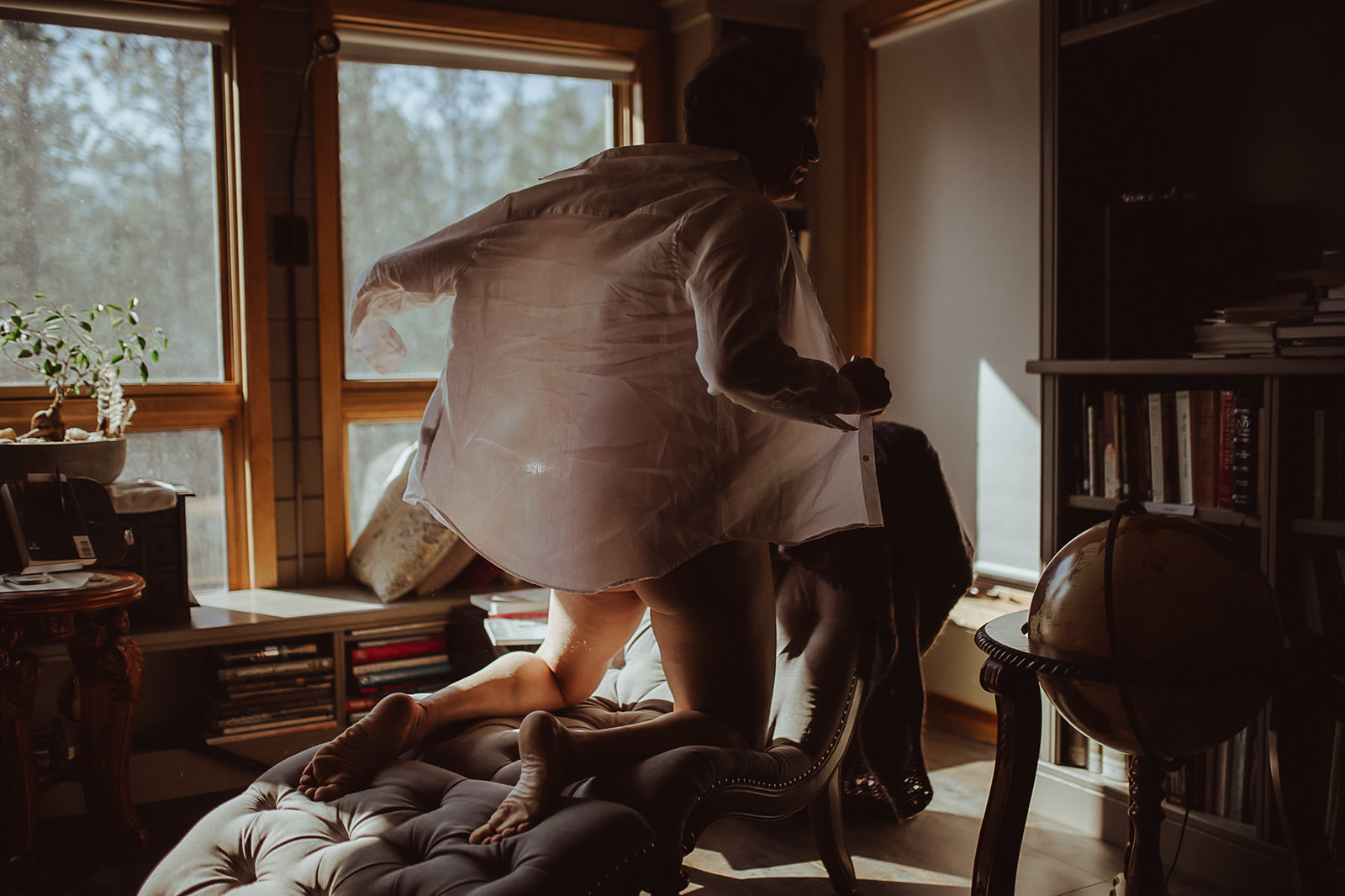 A man kneels on a leather lounge chair taking off his white shirt after visiting boutique hotels in Montana