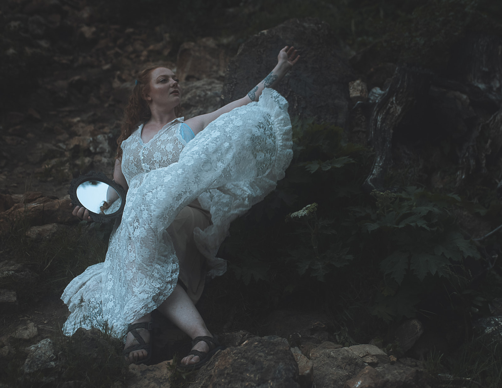 A woman climbs on a waterfall with a mirror in white lace lingerie after visiting bridal shops in Kalispell, MT