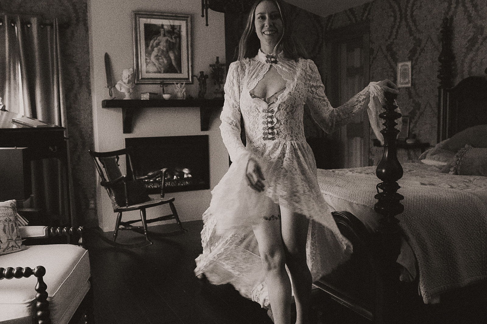 A smiling woman dances in a vintage bedroom wearing a lace corset gown