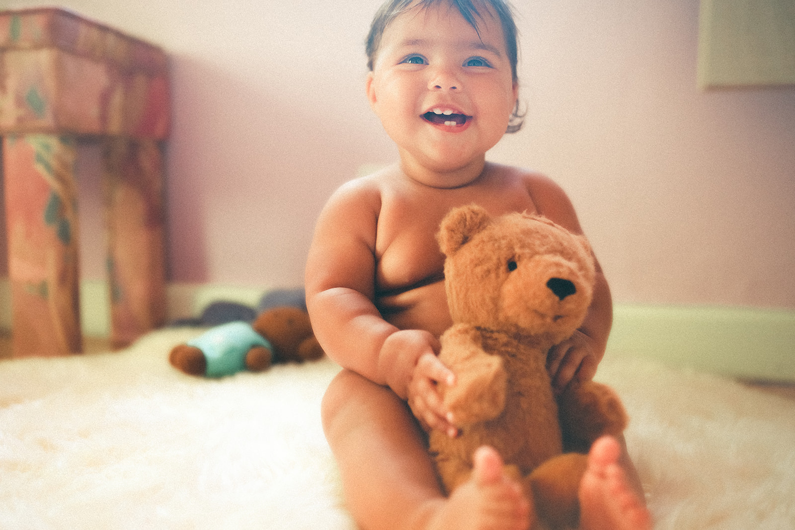A happy baby sits in a nursery with a stuffed ber in her lap after enjoying childcare in Kalispell