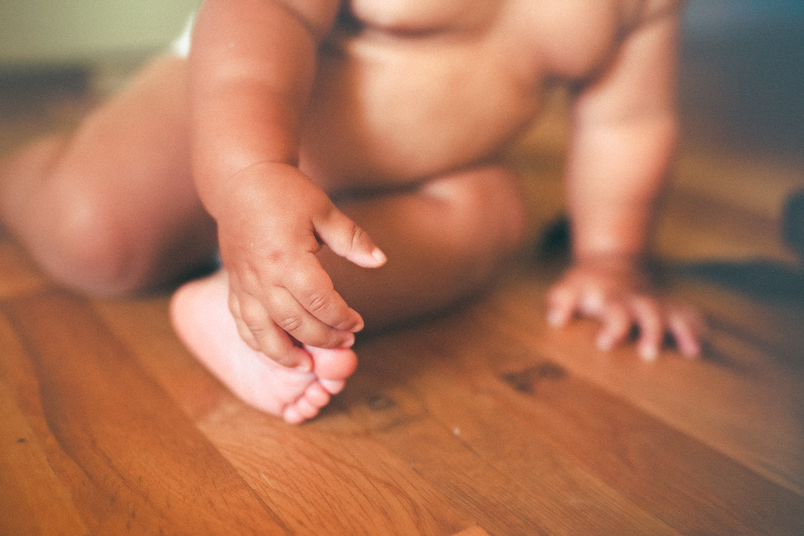Details of a baby's hand touching its foot while sitting on wood floor after using childcare in Kalispell