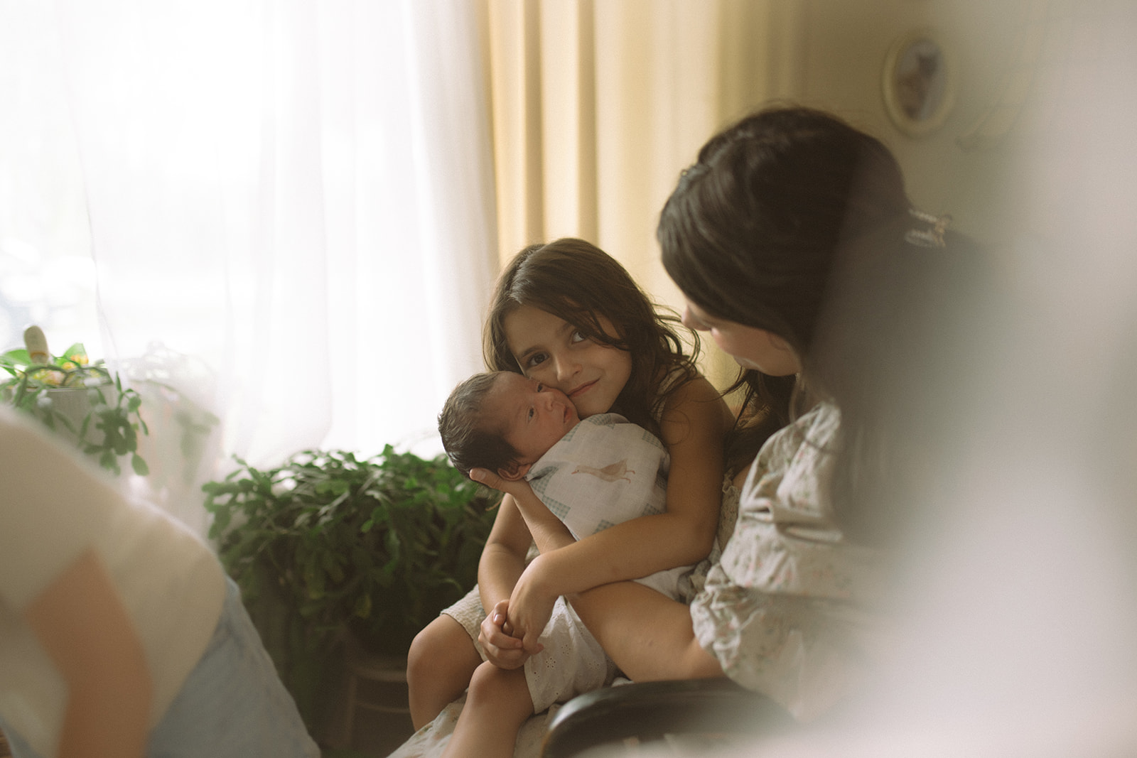 A happy young girl snuggles her newborn sibling in mom's lap thanks to support from Community Medial Center PICU